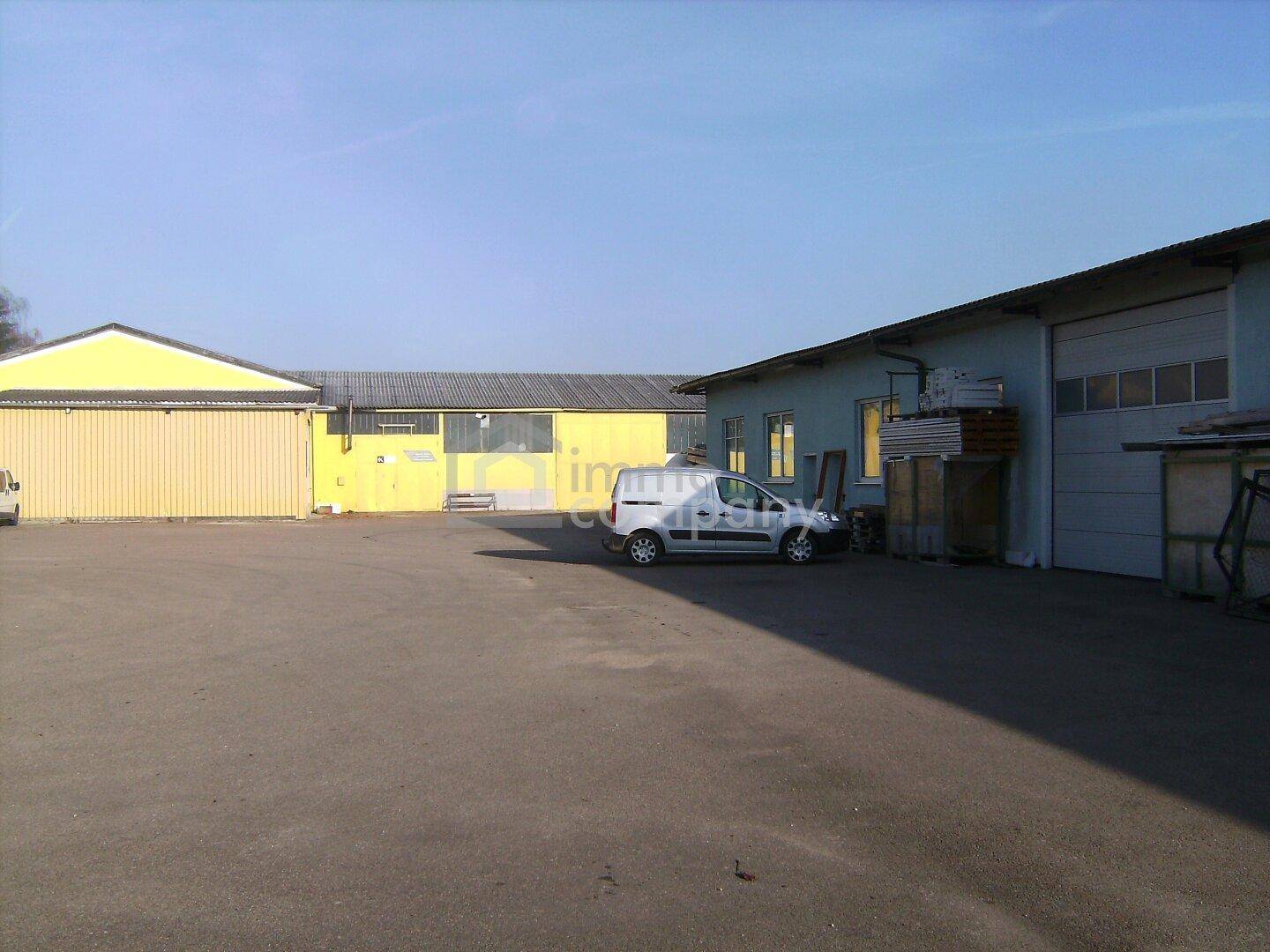 Weitläufiger Außenbereich mit mehreren Industriegebäuden und einer großen asphaltierten Parkfläche mit einem Lieferwagen.