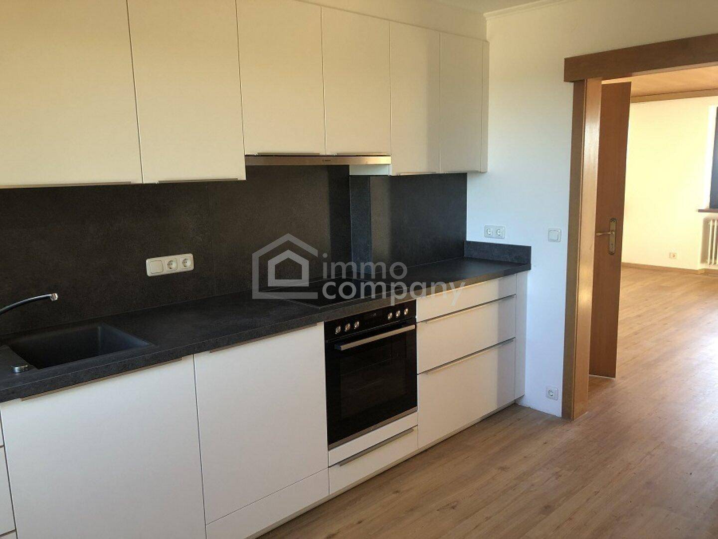 Moderne Einbauküche mit weißen Schränken, dunkler Arbeitsplatte und Holzboden.