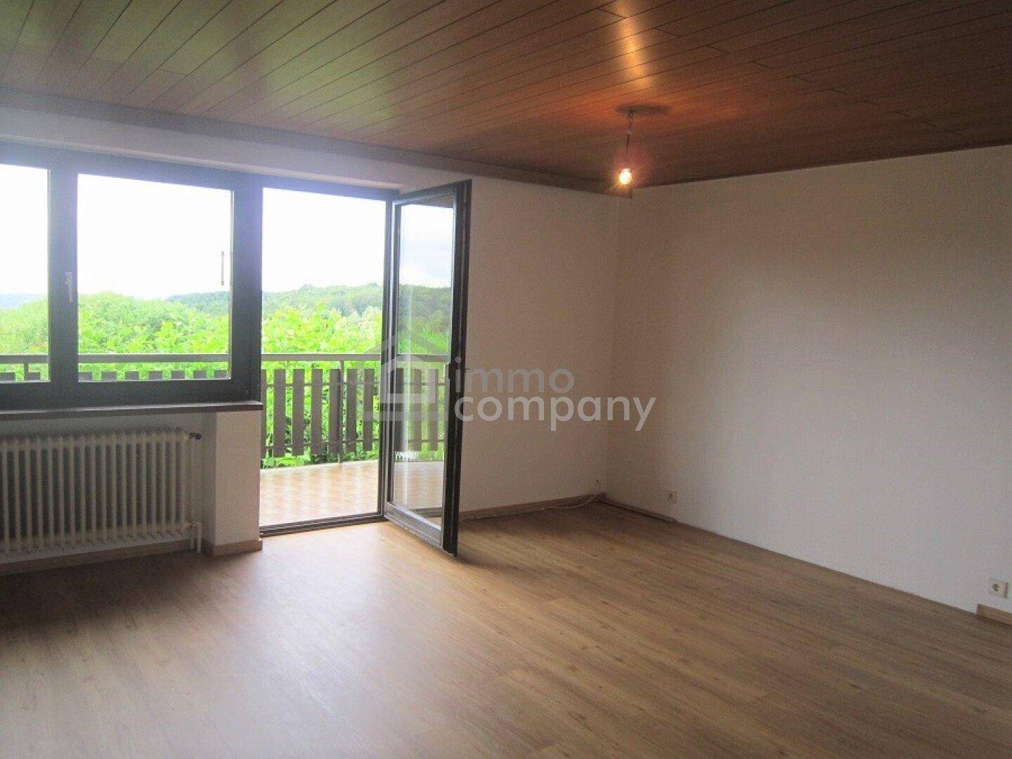 Helles Wohnzimmer mit Holzboden, Holzdecke und Zugang zu einem Balkon mit Weitblick.