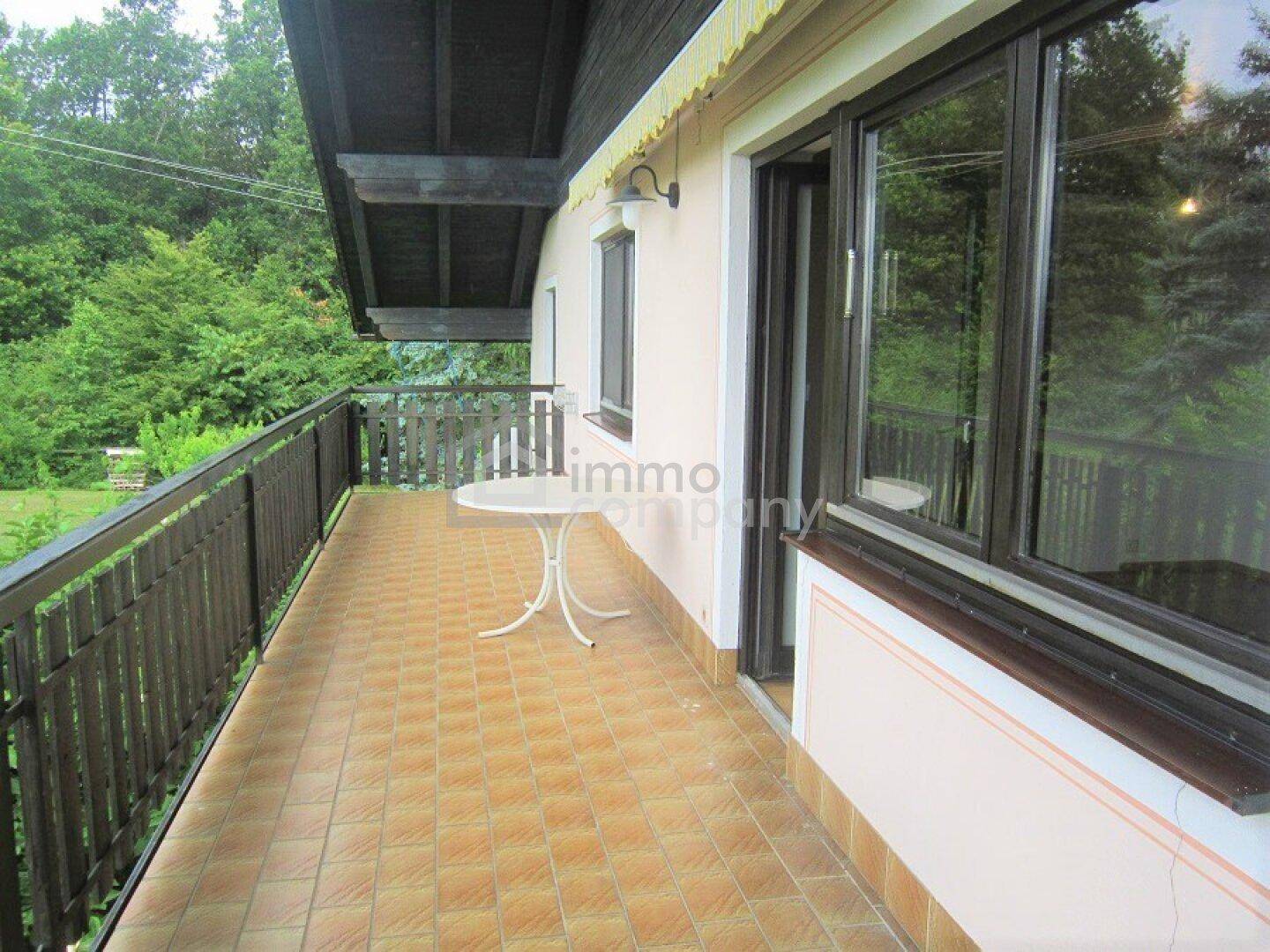 Gefliester Balkon mit kleinem Tisch und Stühlen, umgeben von viel Grün.