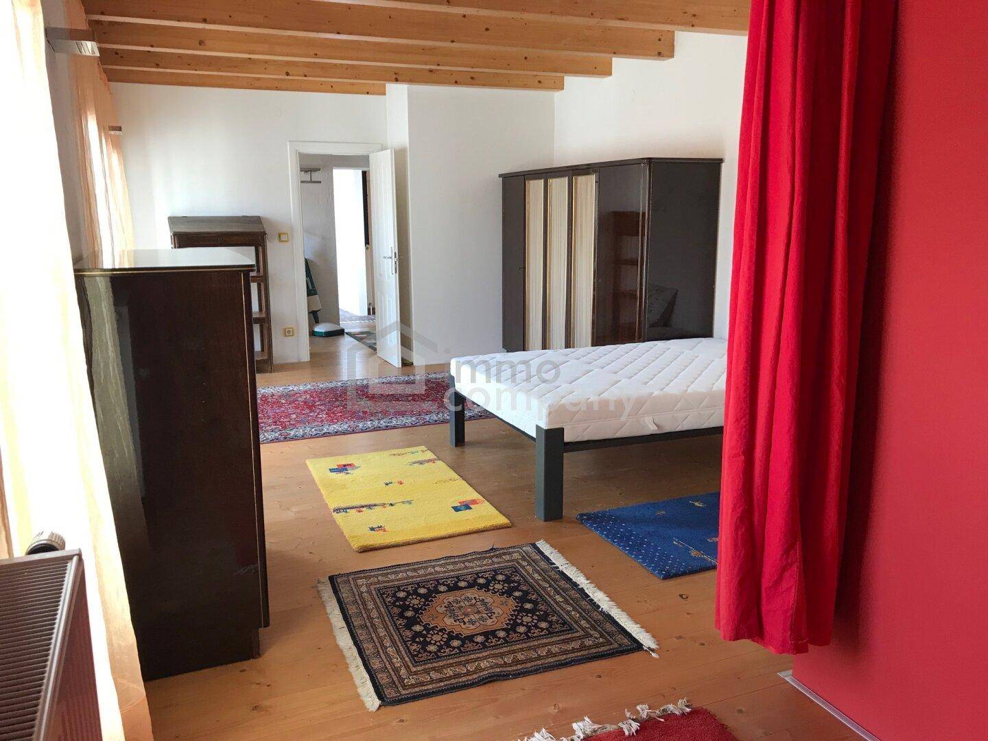 Geräumiges Schlafzimmer mit Holzboden, einem Bett und einem Kleiderschrank, durch einen roten Vorhang abgetrennt.