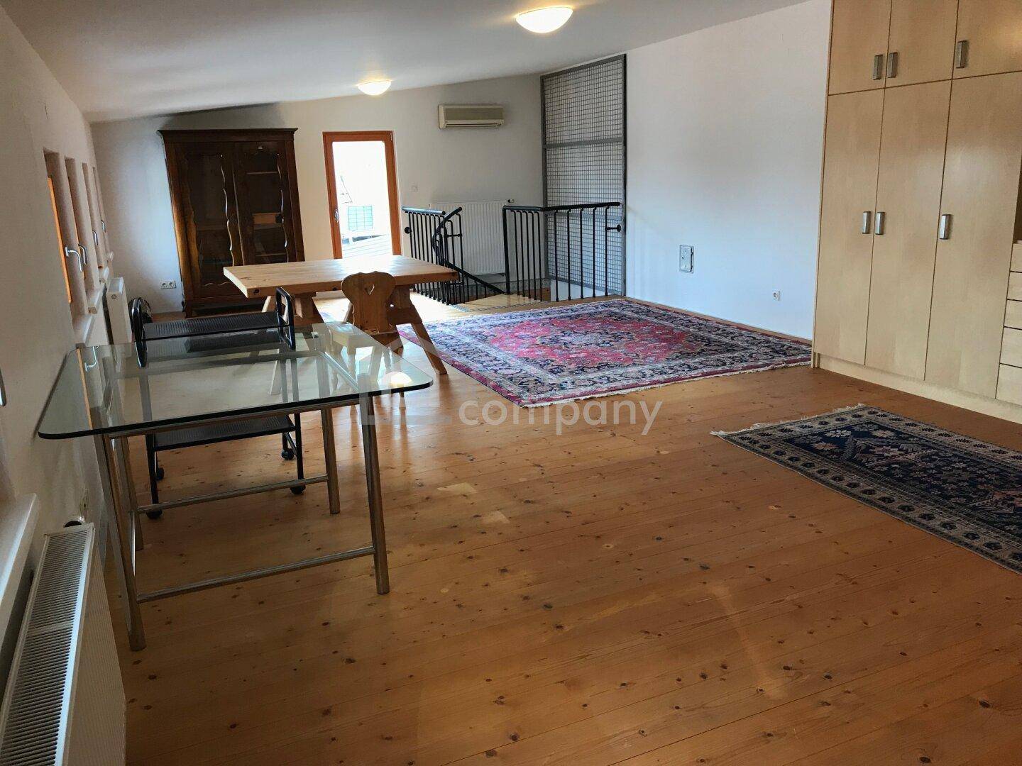 Heller offener Wohnbereich mit Holzboden, Einbauschränken und einer Treppe zu einer oberen Ebene.