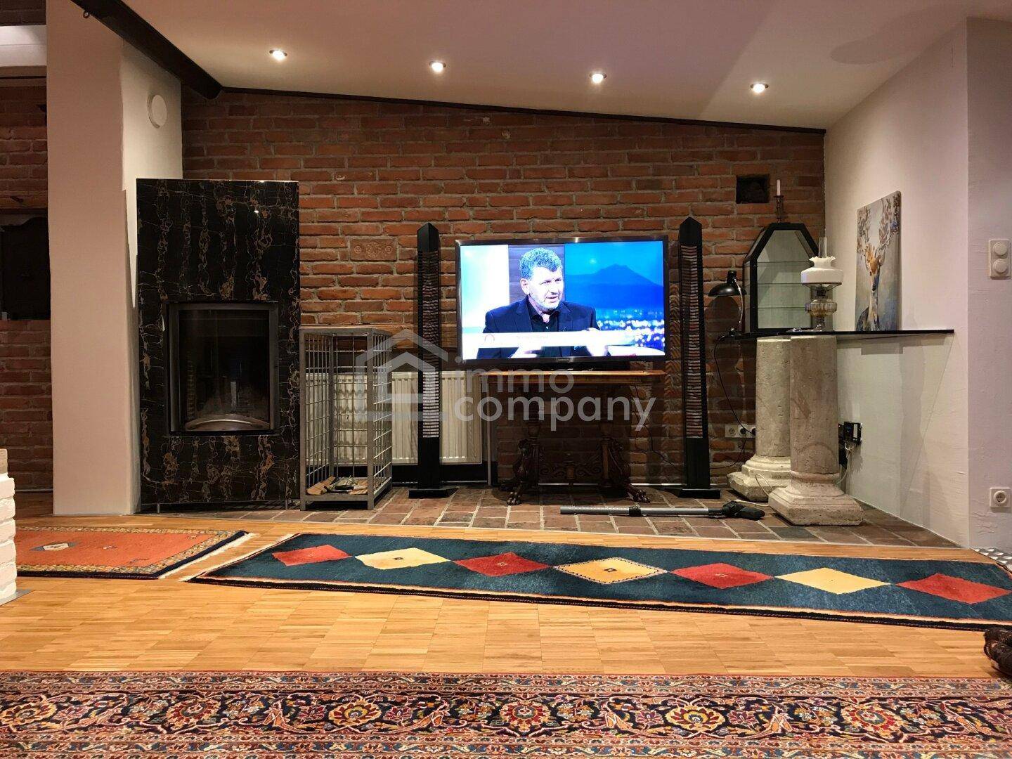 Wohnzimmer mit großem Fernseher, Kaminofen und dekorativen Säulen vor einer Ziegelwand.