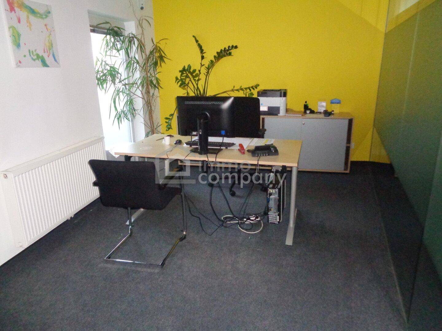 Ein modern eingerichtetes Büro mit gelber Akzentwand, Schreibtisch und Bürostuhl.