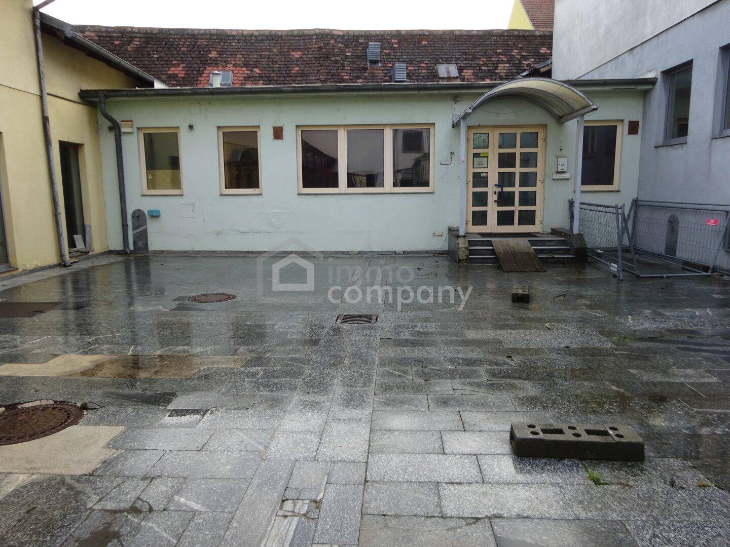 Hinterhof mit gepflastertem Boden und einem Gebäude mit Rampe und Eingang.