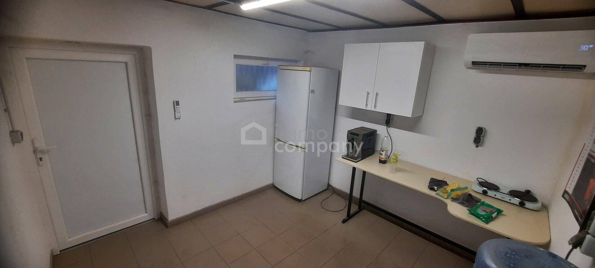 Kleine Küchenzeile mit Kühlschrank, Hängeschränken, Arbeitsplatte und Kochfeld, ideal für Pausen.