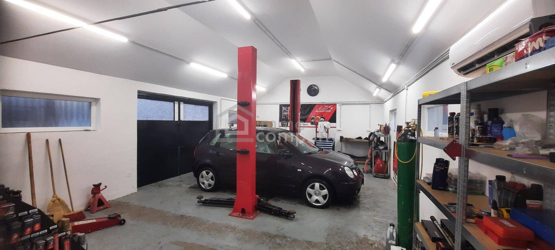 Geräumige Werkstatt mit Hebebühne, einem Auto und heller Beleuchtung, ideal für Fahrzeugreparaturen.