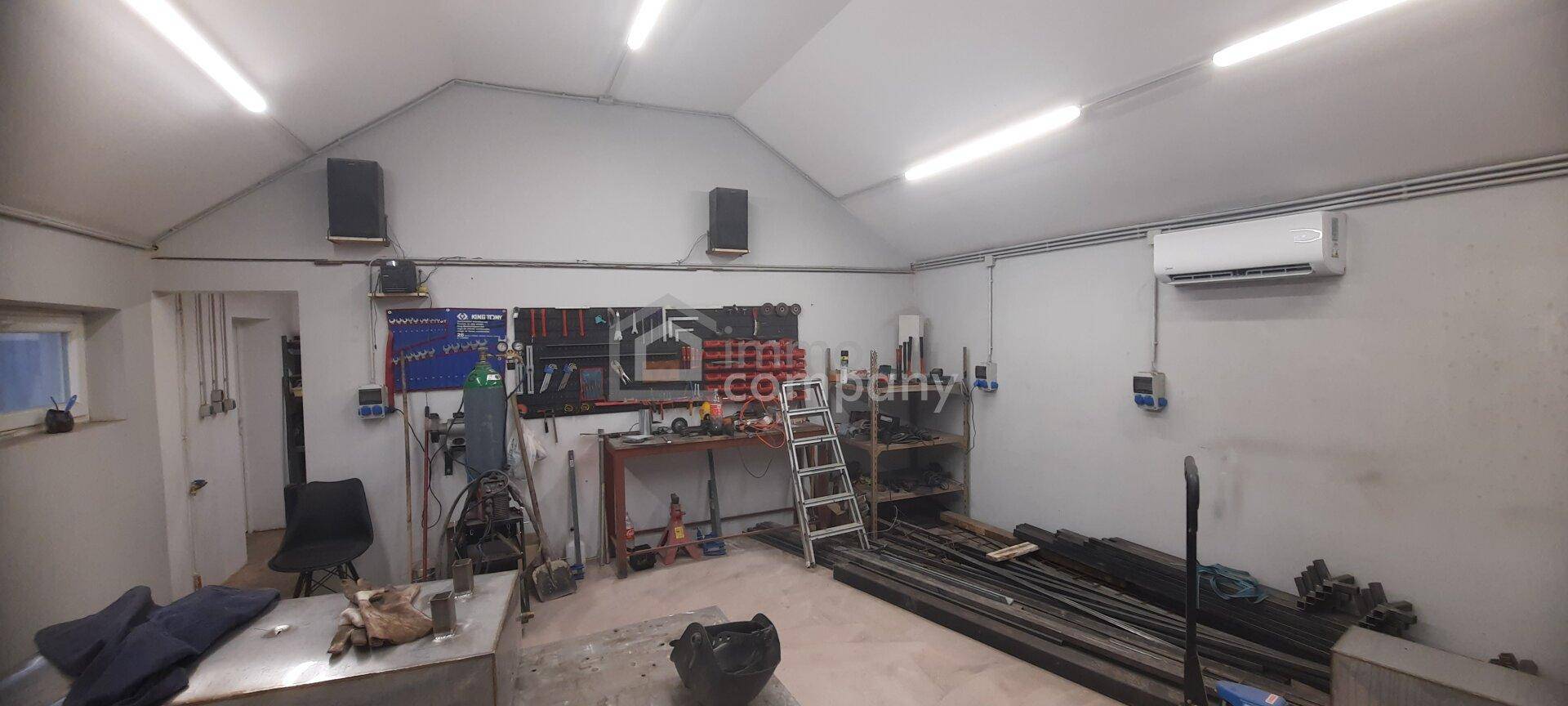 Werkstattbereich mit umfangreicher Werkzeugwand, einer Werkbank, Lautsprechern und einem Klimagerät an der Wand.