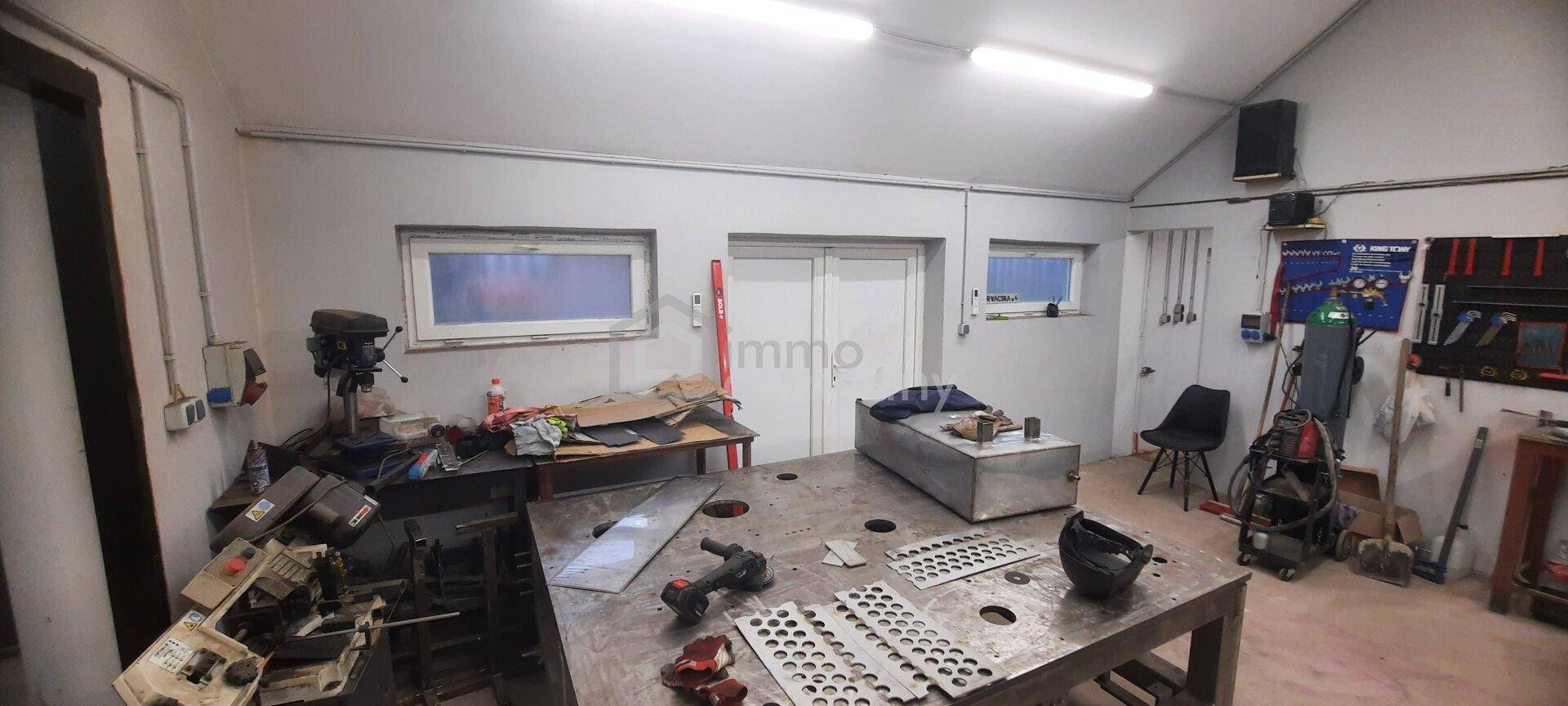 Geräumiger Werkstattbereich mit großer Metallwerkbank, verschiedenen Werkzeugen und Fenstern für Tageslicht.