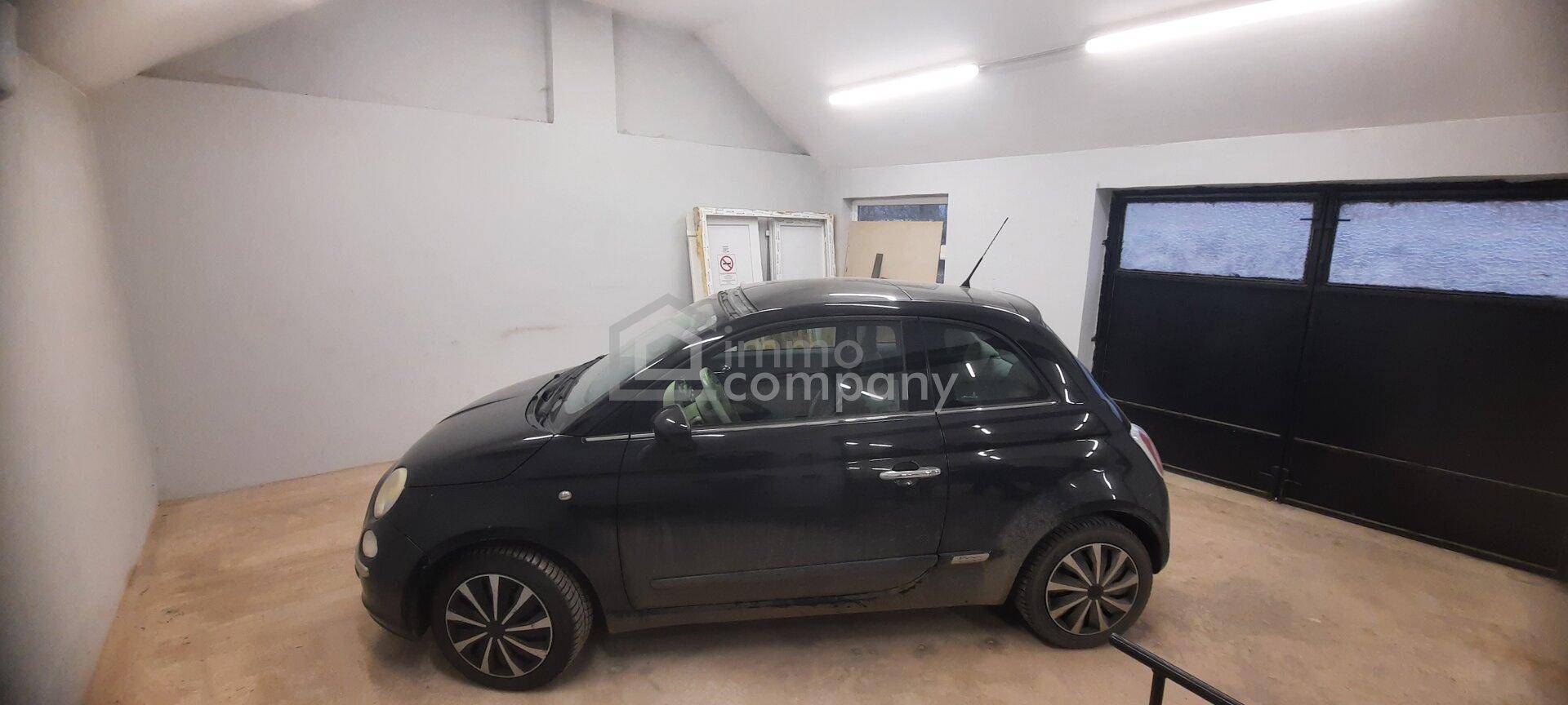 Helle Garage mit einem schwarzen Kleinwagen, einem großen Garagentor und einem einfachen Betonboden.