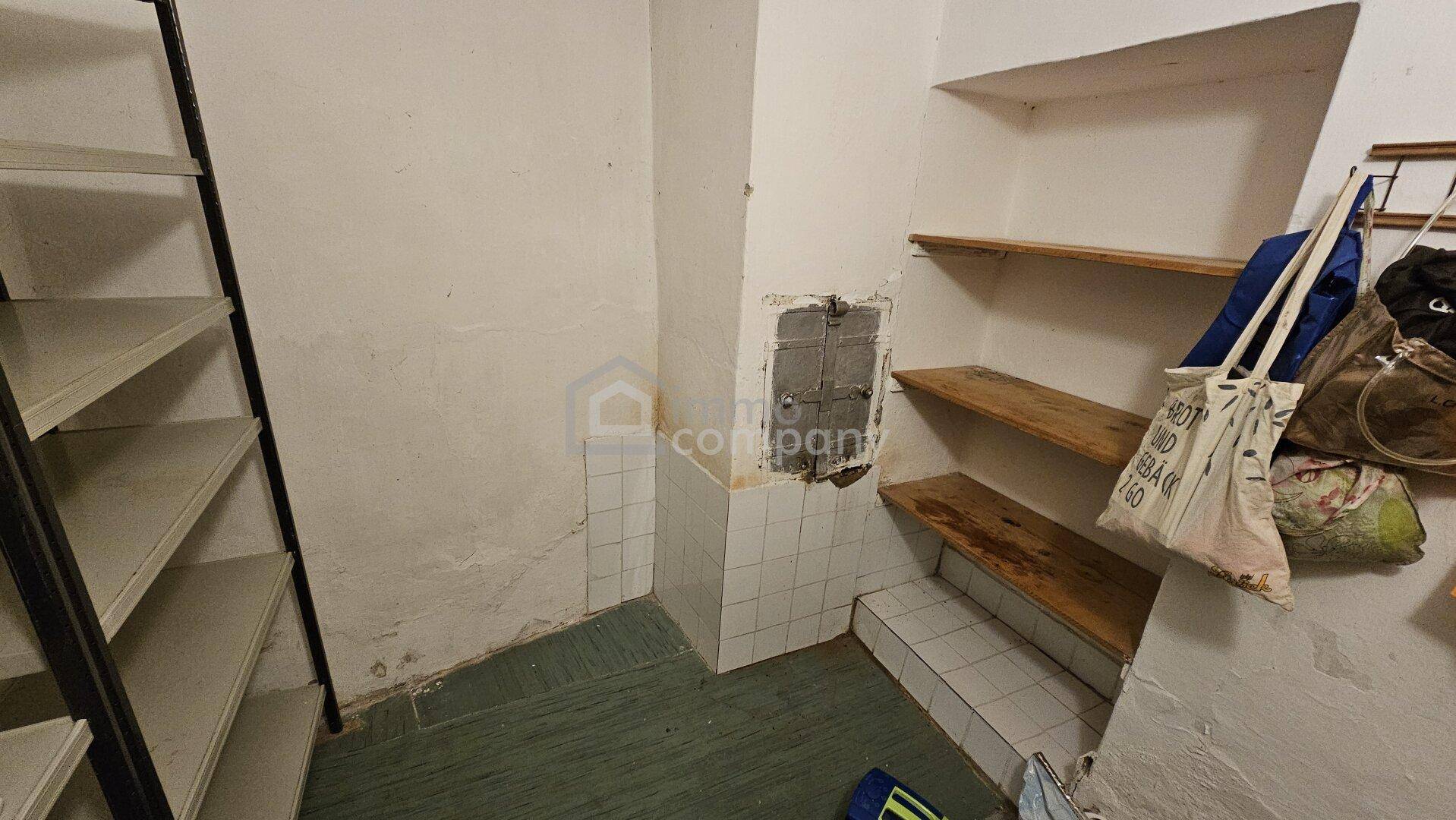 Einfacher Abstellraum mit Regalen, gefliesten Wänden im unteren Bereich und Betonboden.