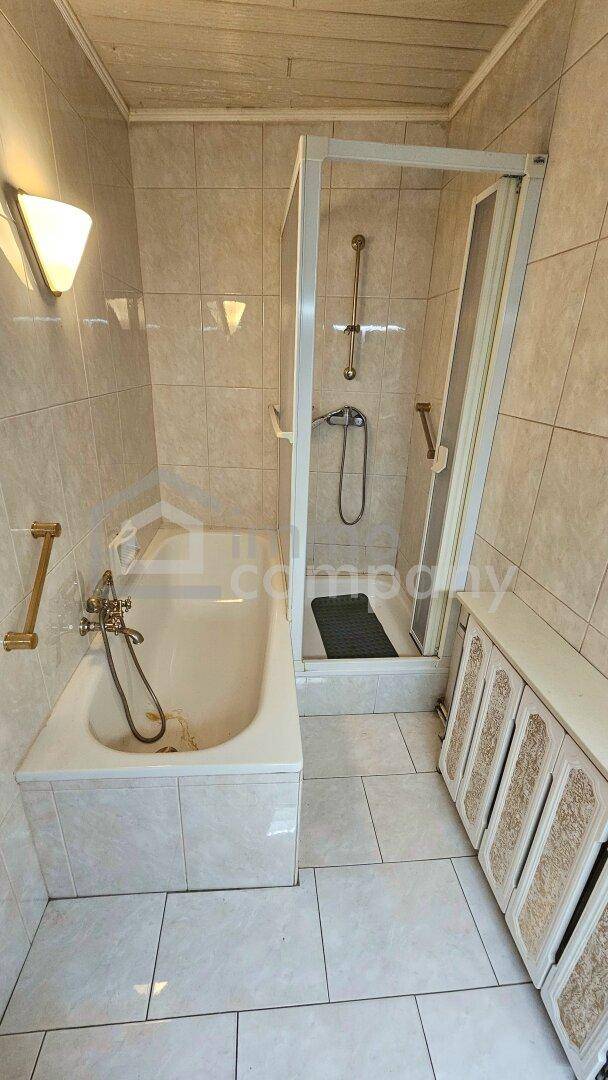Badezimmer mit Badewanne, Duschkabine und hellen Fliesen in gutem Zustand.