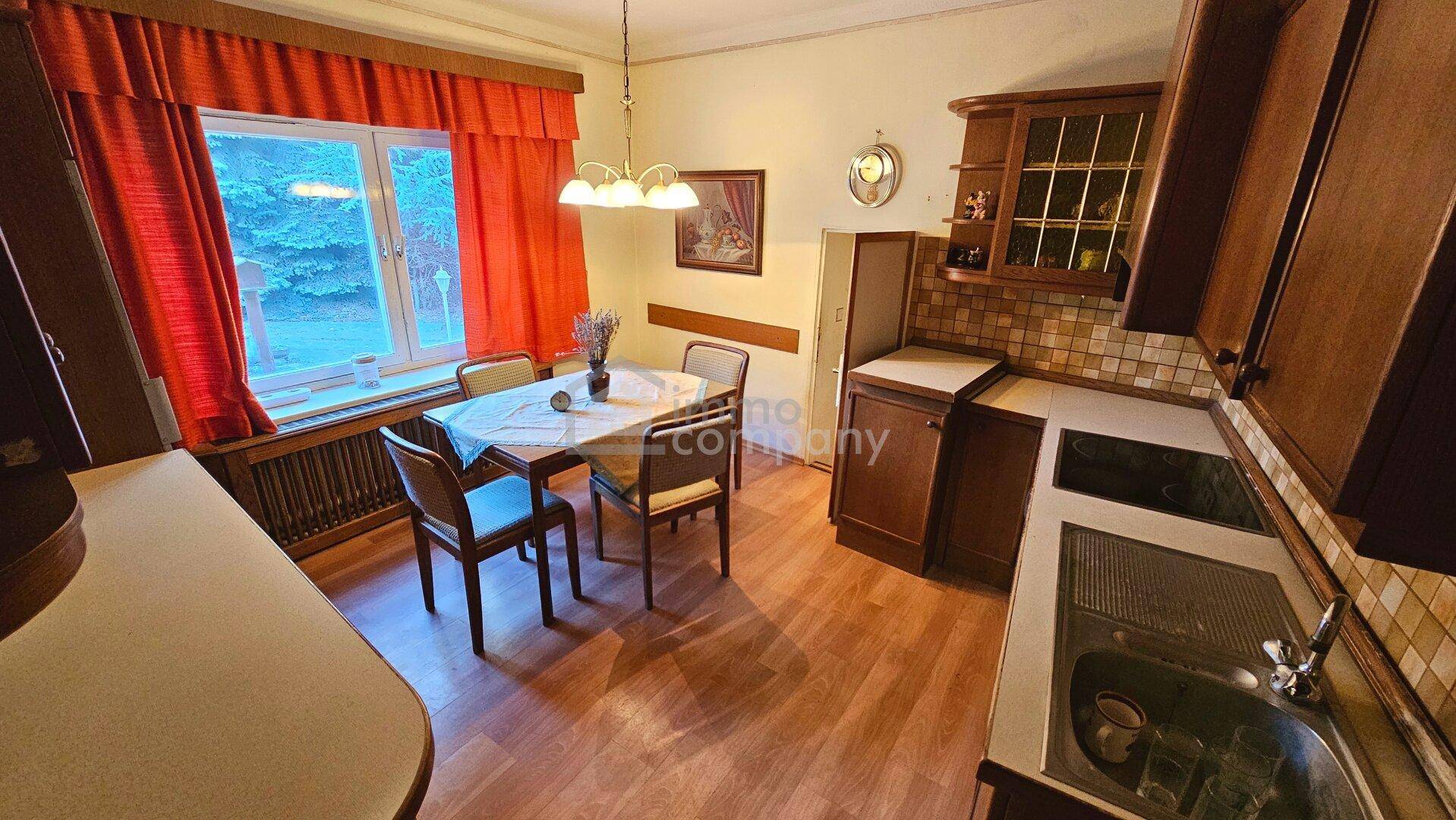 Wohnküche mit Holzeinbauten, Esstisch und Fenster mit roten Vorhängen in traditionellem Stil.