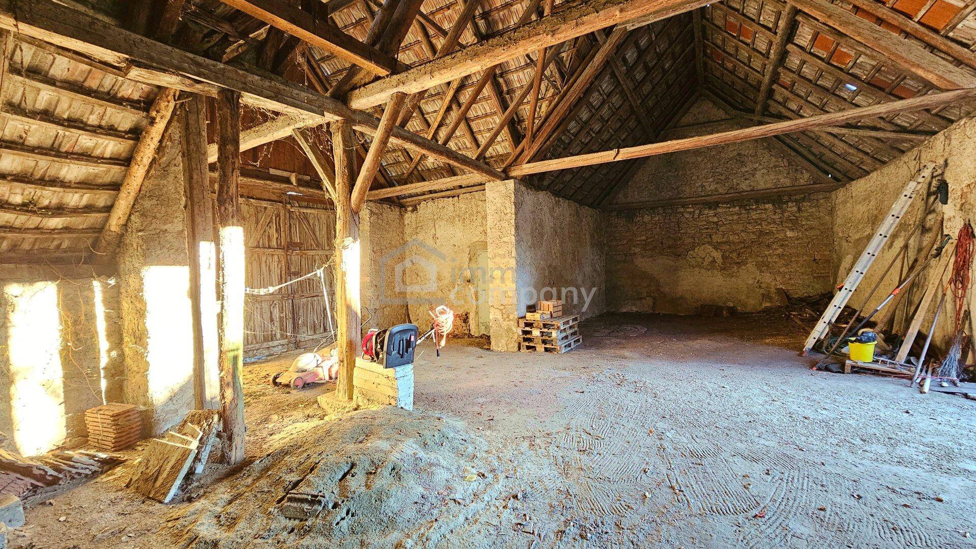 Großer, rustikaler Scheunen- oder Dachbodenraum mit sichtbaren Holzbalken und Steinmauern.