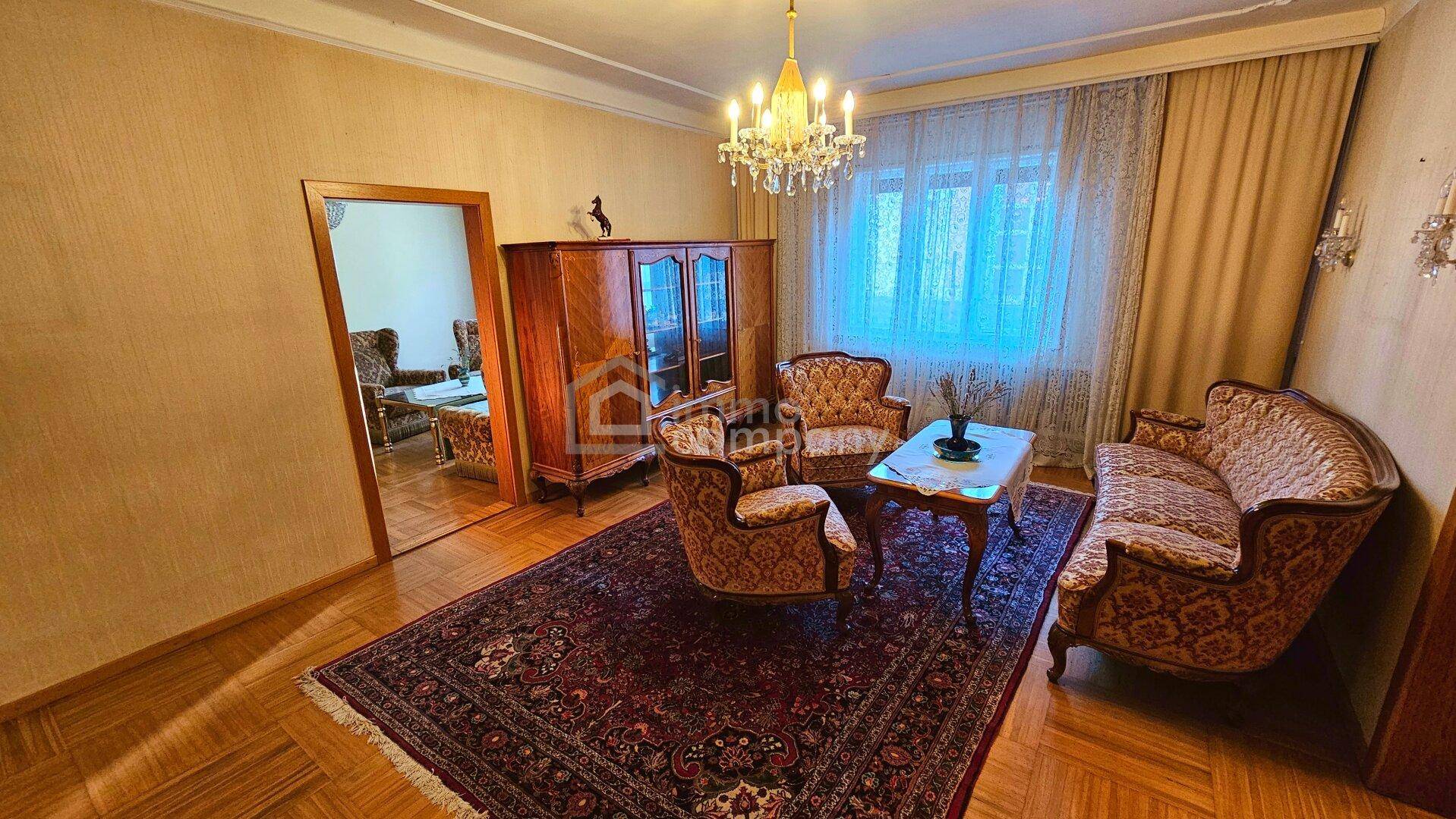 Traditionelles Wohnzimmer mit klassischem Mobiliar, großem Fenster, Kronleuchter und Parkettboden.