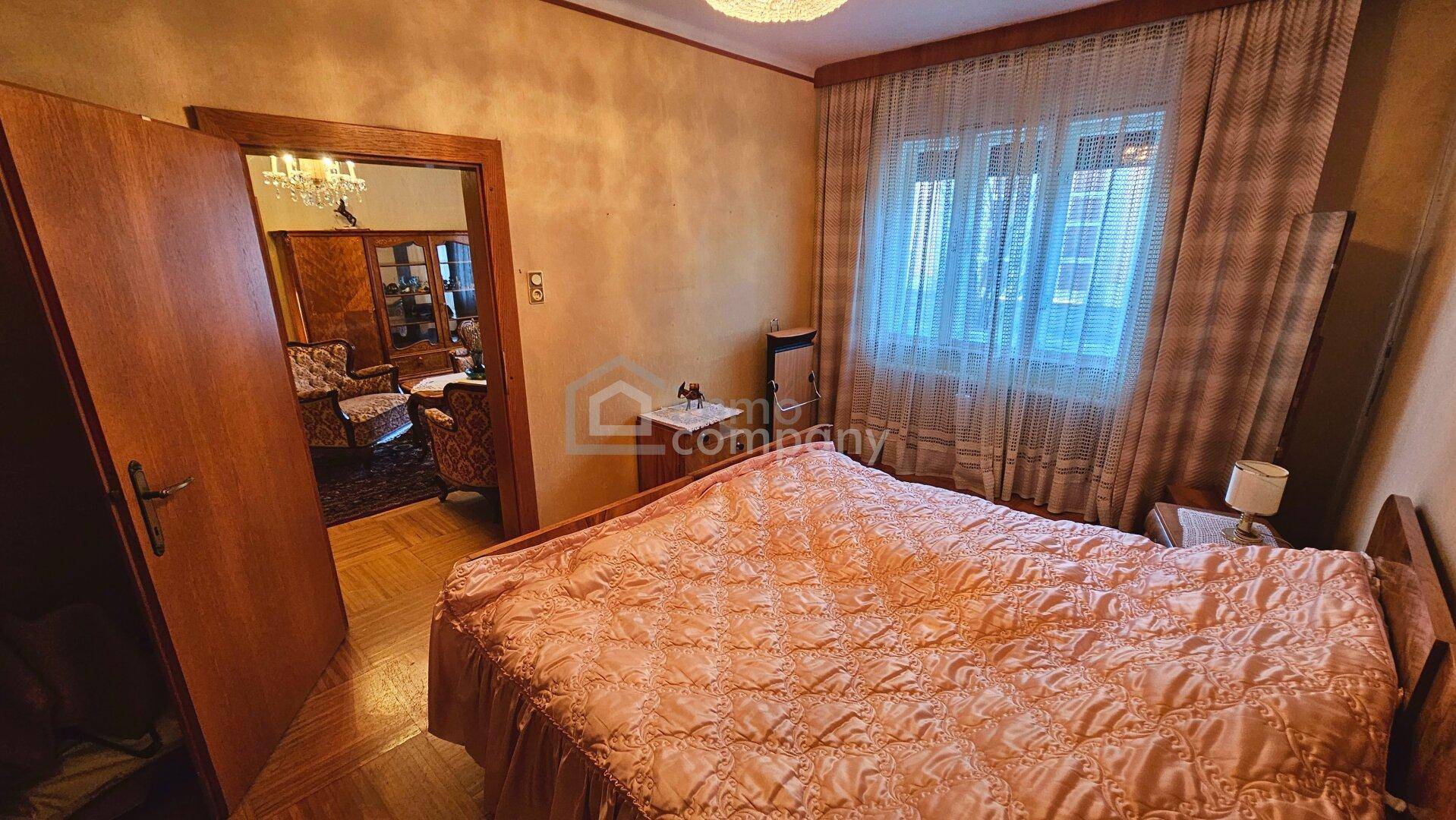 Schlafzimmer mit Doppelbett, einfacher Einrichtung und Fenster mit Vorhängen in traditionellem Stil.