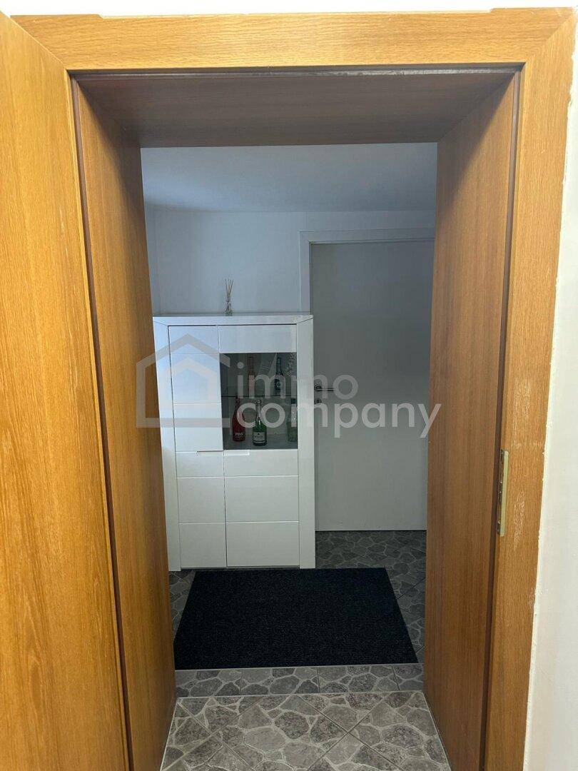 Blick durch eine Holztür in einen kleinen, schlichten Raum mit weißem Schrank und dunkler Matte.