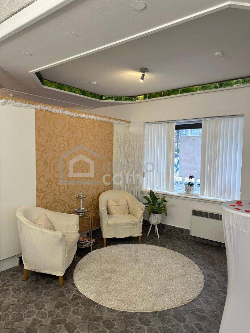 Gemütlicher Wartebereich mit zwei beigen Sesseln, Fenster mit Jalousien und dekorativer Decke.