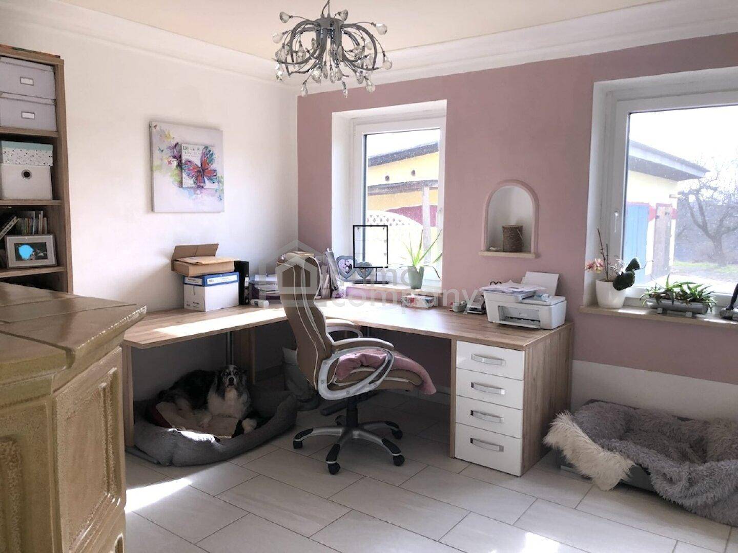 Helles Büro mit großem Schreibtisch, Fliesenboden und rosa Akzentwand.