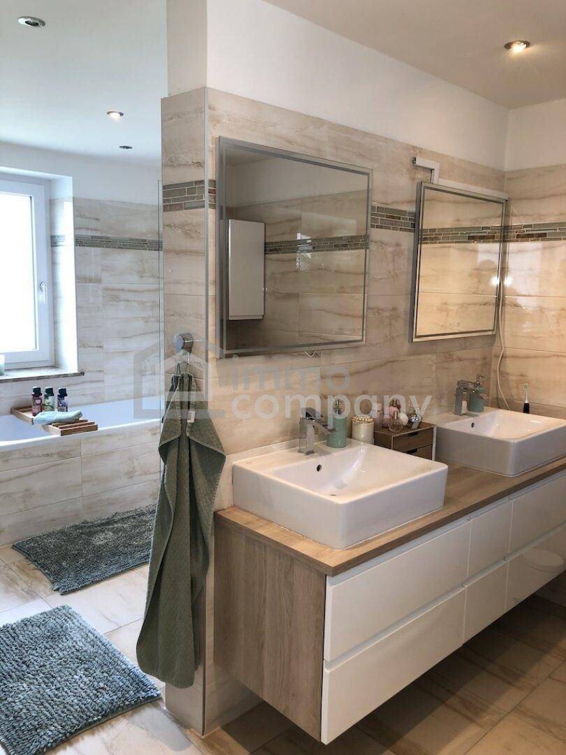 Modernes Badezimmer mit Doppelwaschbecken, großen Fliesen und Badewanne im Hintergrund.