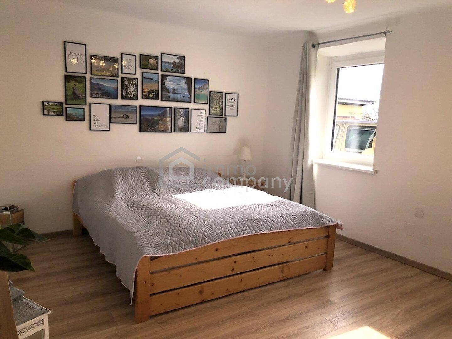 Schlafzimmer mit Holzbett, Laminatboden und einer Bildergalerie an der Wand.