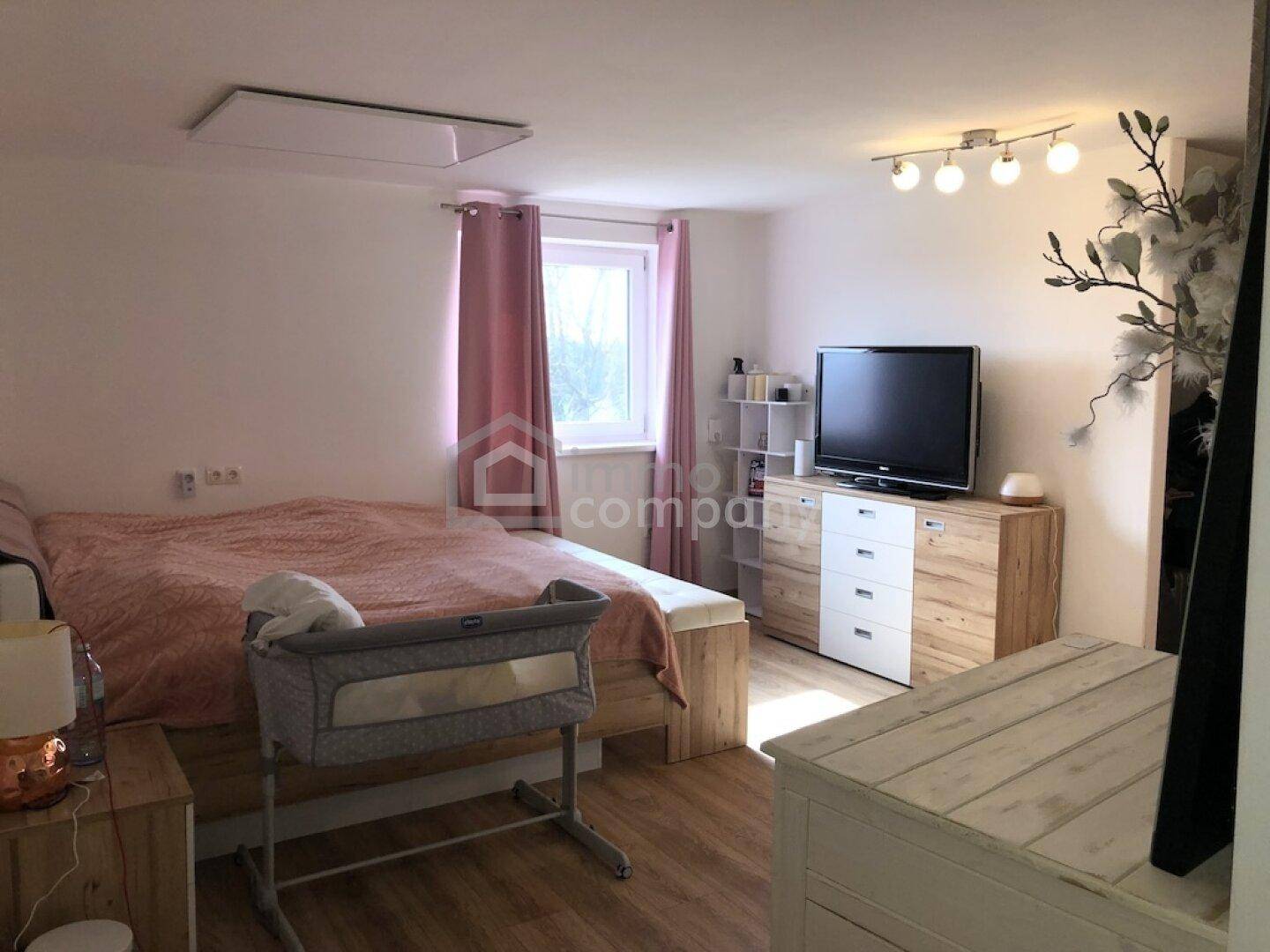 Schlafzimmer mit Doppelbett, Laminatboden und einem Babybettchen.