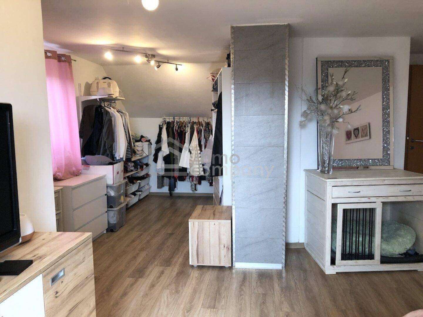 Schlafzimmer mit Ankleidebereich, Laminatboden und einem großen Spiegel.