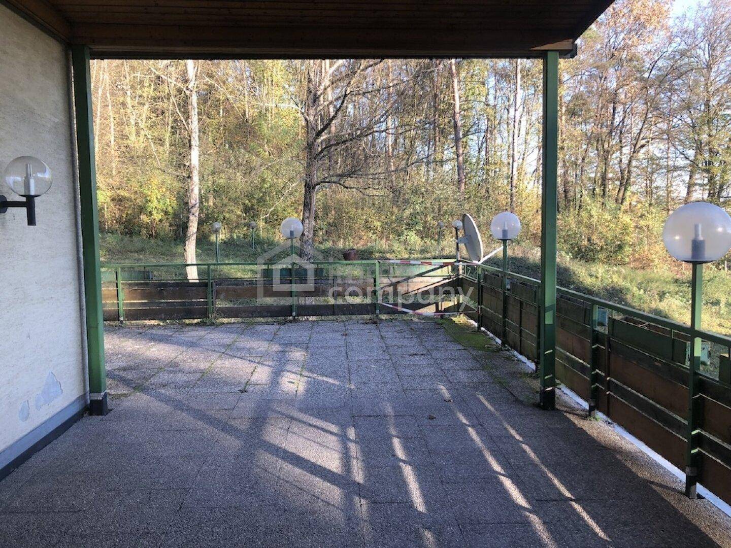 Geräumige, gepflasterte Terrasse mit Geländer und weitem Blick ins Grüne und auf Bäume.