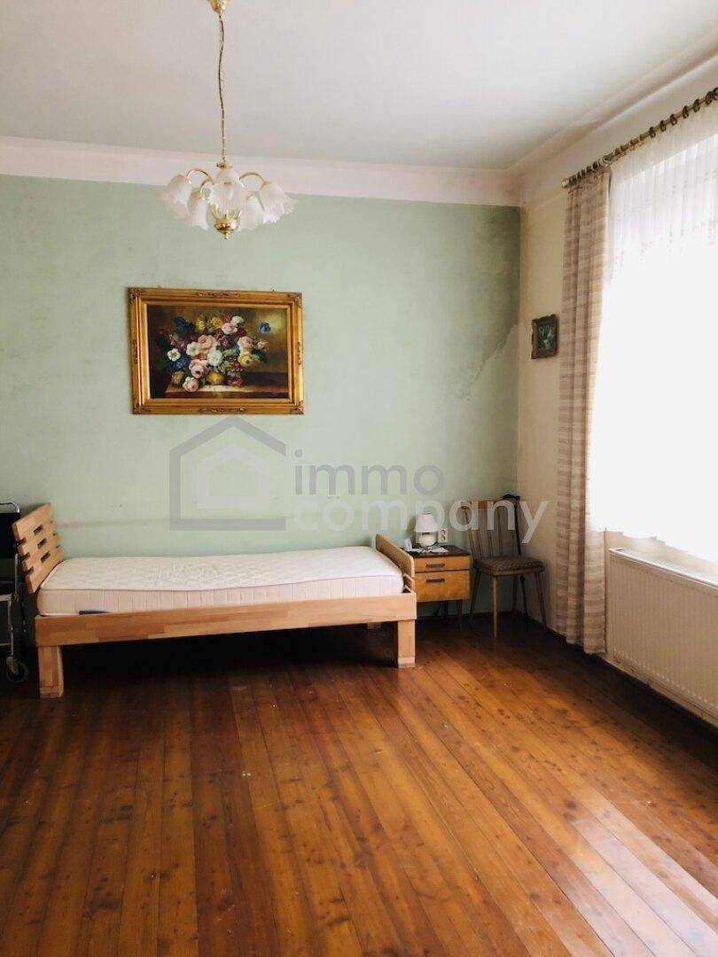 Helles Schlafzimmer mit Holzboden, einfacher Einrichtung und hellgrünen Wänden in einem Altbau.