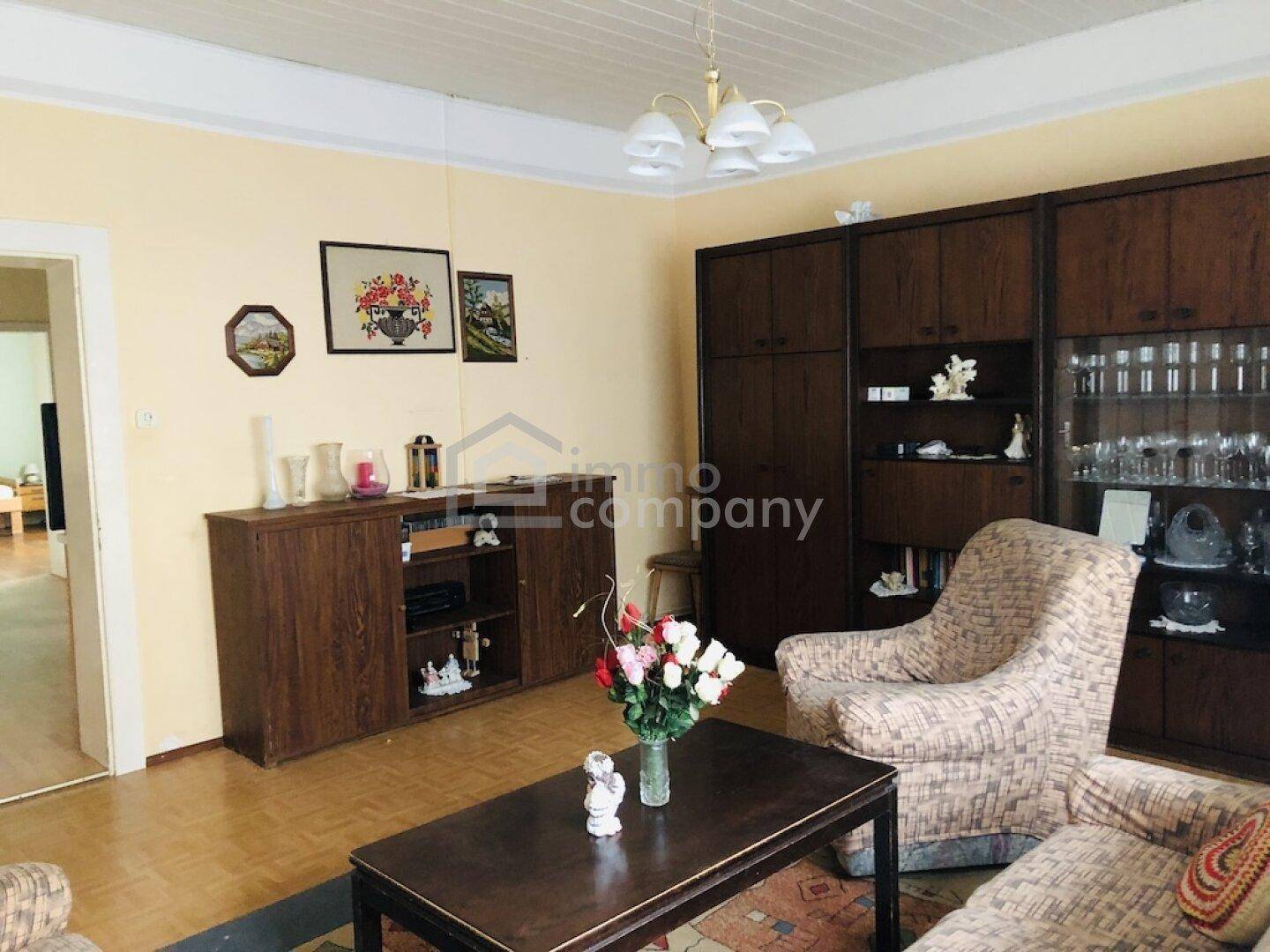 Gemütliches Wohnzimmer mit traditionellen Holzmöbeln, Teppich und gelblichen Wänden in einem Altbau.