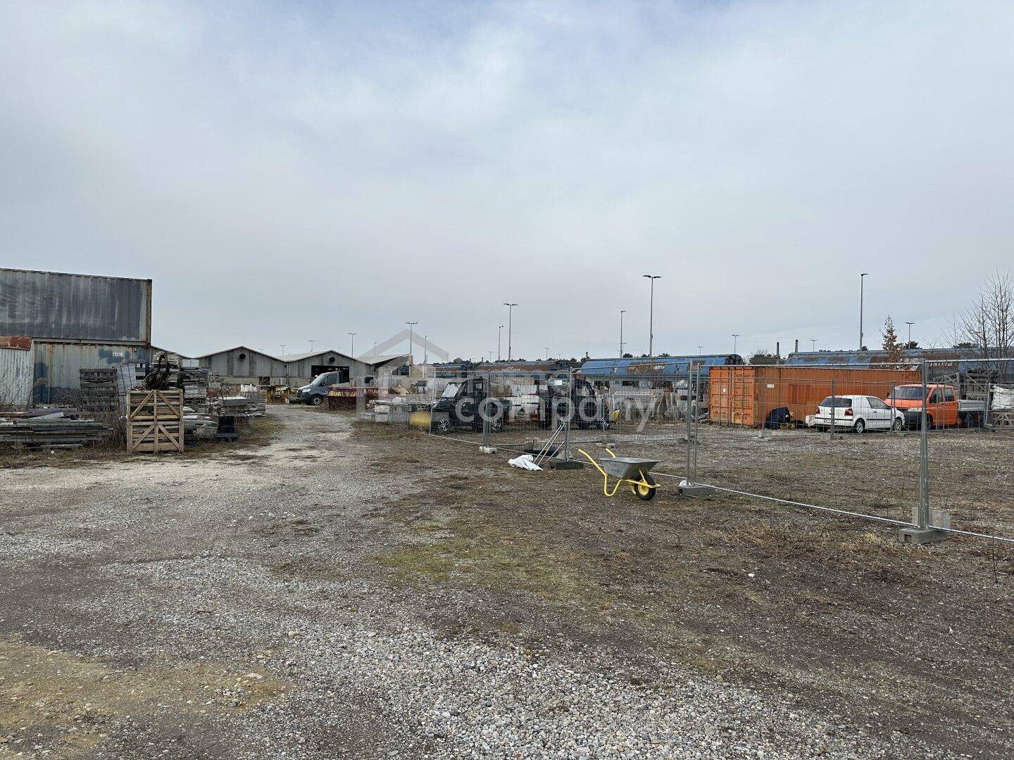 Großes, unordentliches Außengelände mit Schotter, industriellen Materialien und mehreren Fahrzeugen unter bewölktem Himmel.