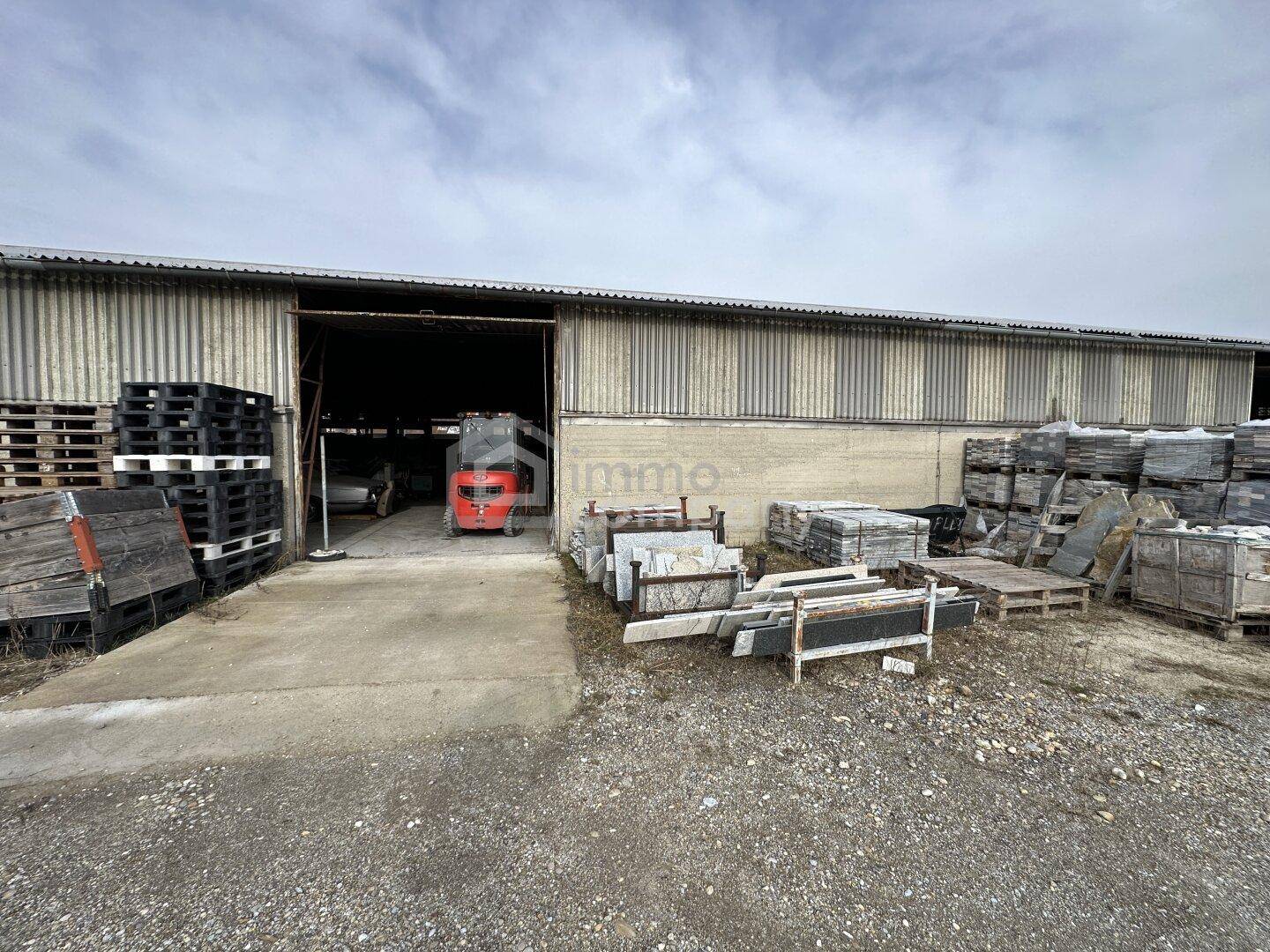 Außenansicht einer Industriehalle mit Wellblechfassade, Gabelstapler im Eingang und gestapelten Steinplatten davor.