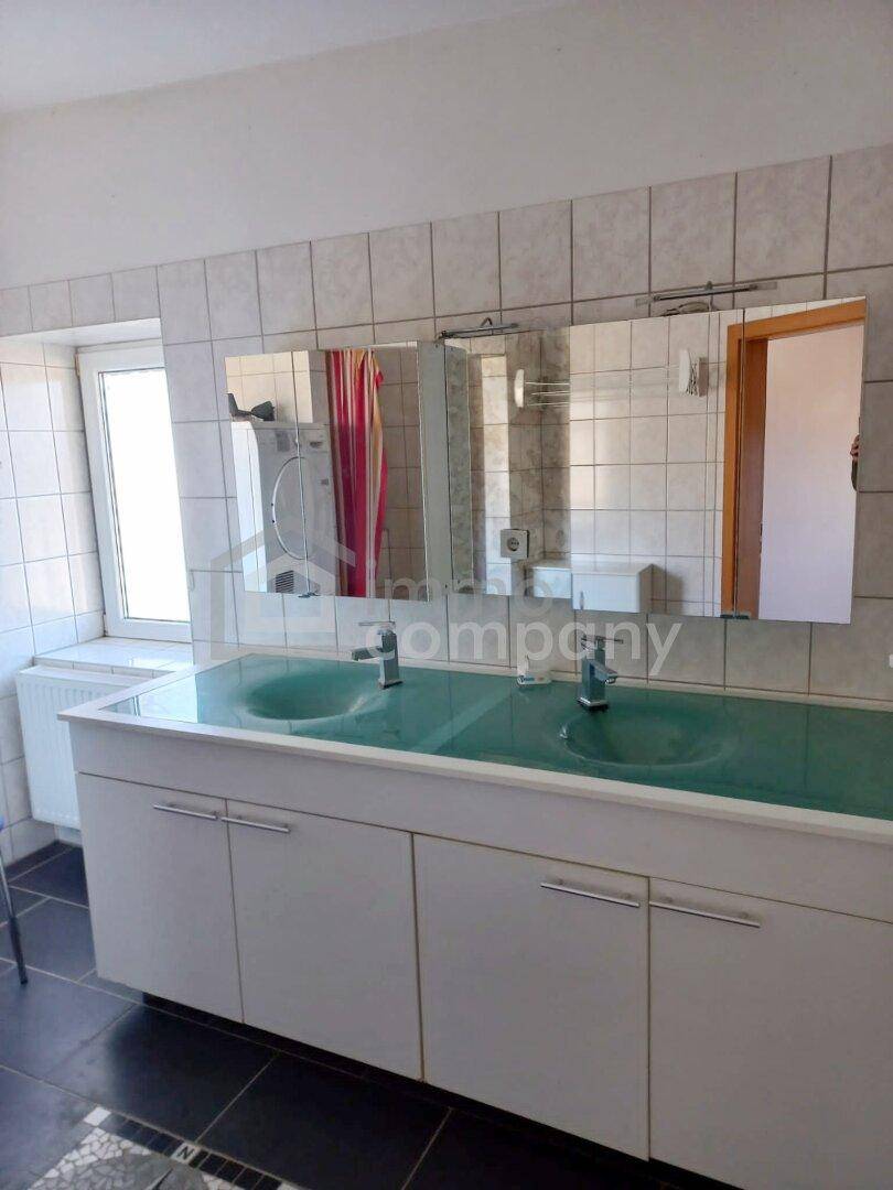 Badezimmer mit Doppelwaschbecken, Spiegelschrank und Fliesen an Wänden und Boden.