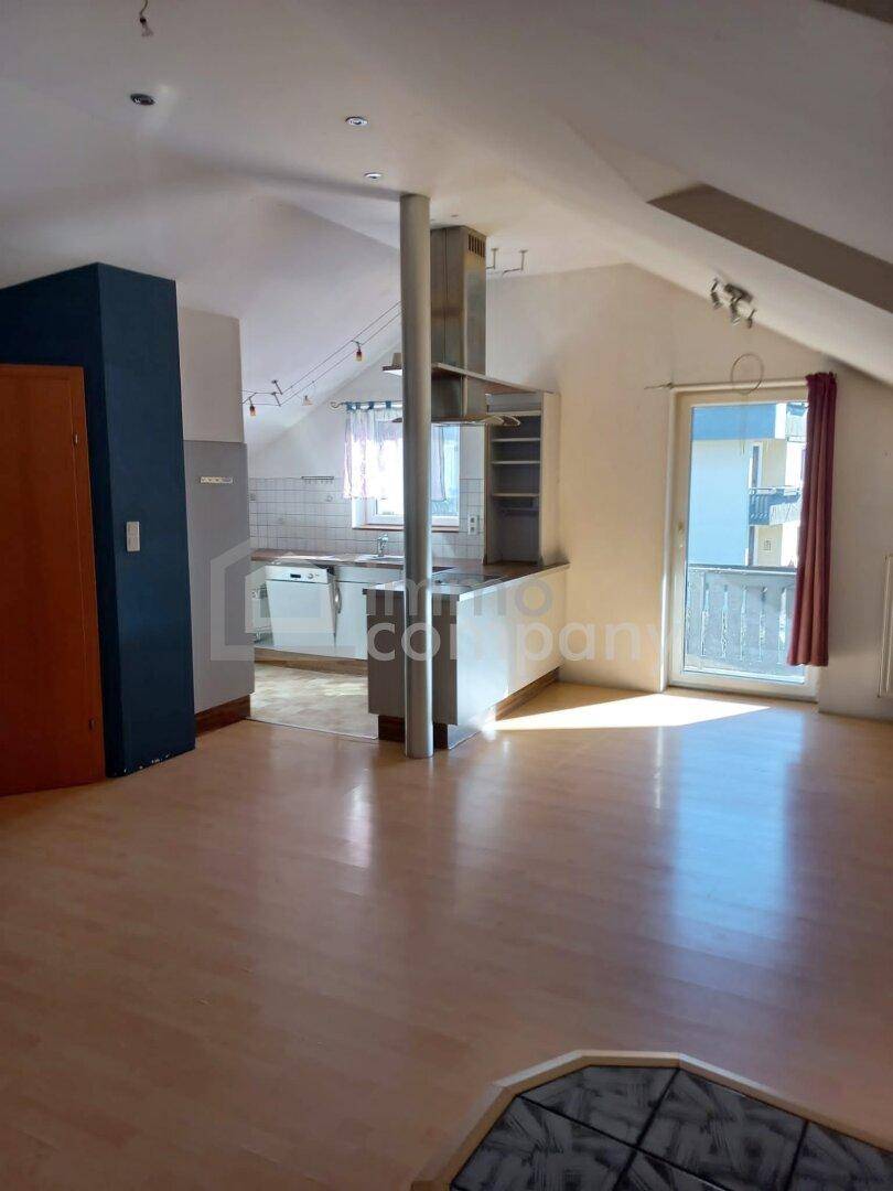 Offener Wohnbereich mit integrierter Küche, Laminatboden und Zugang zum Balkon.