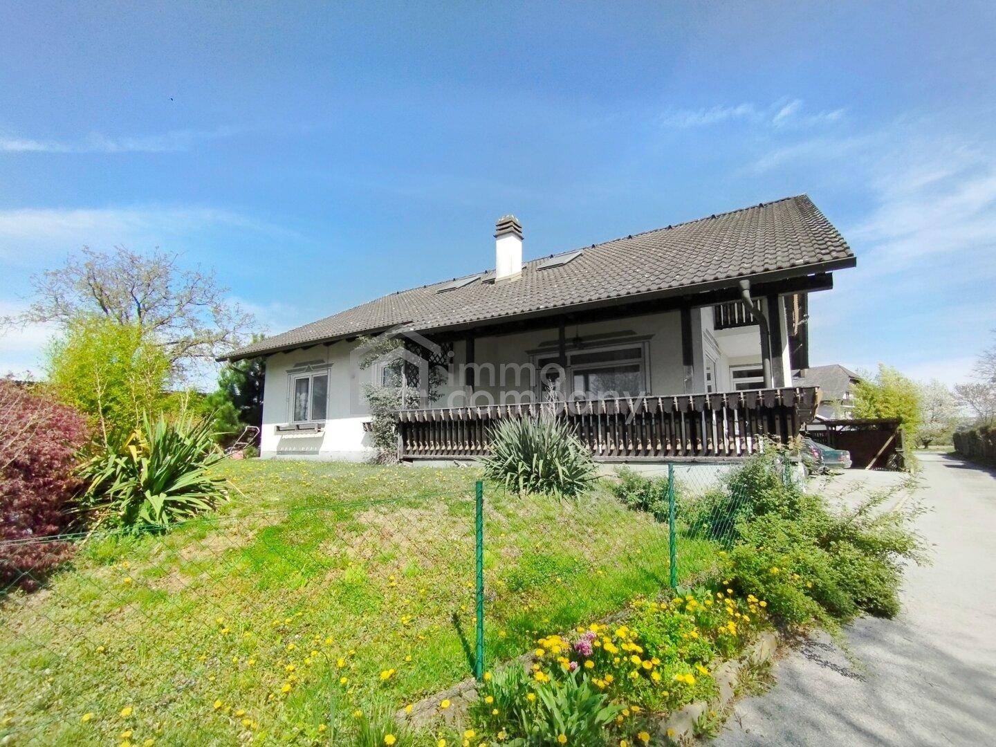 Freistehendes Haus mit großem Garten und einer Holzterrasse unter blauem Himmel.