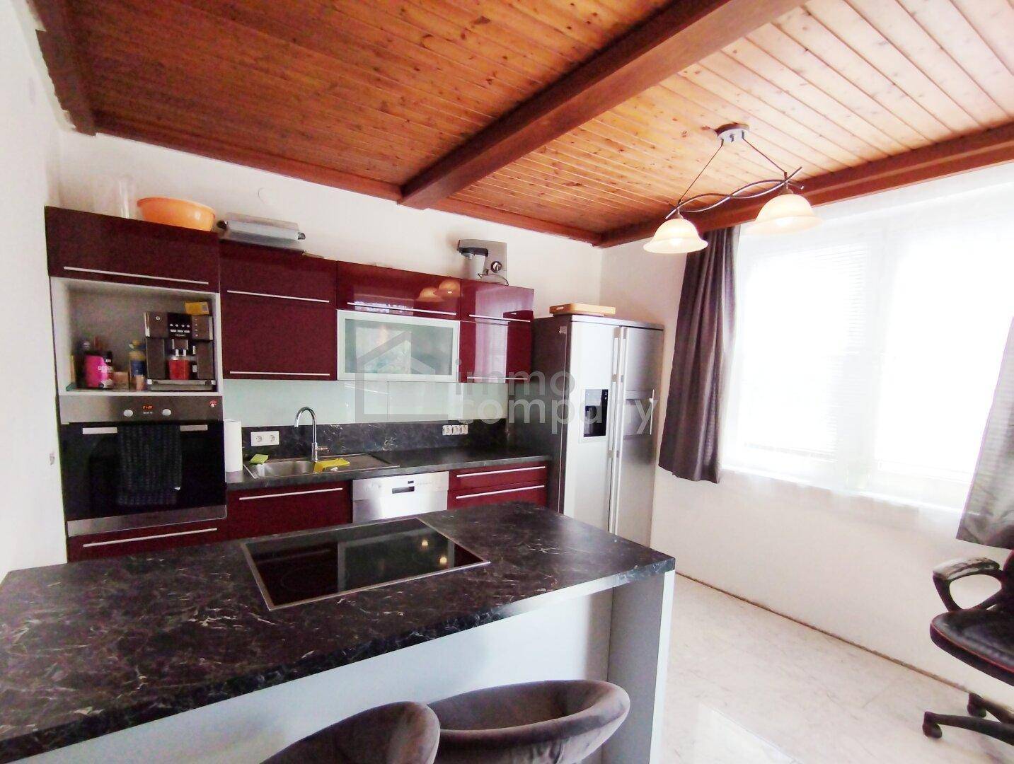 Moderne Küche mit dunkelroten Hochglanzschränken, dunkler Arbeitsplatte und Holzbalkendecke.