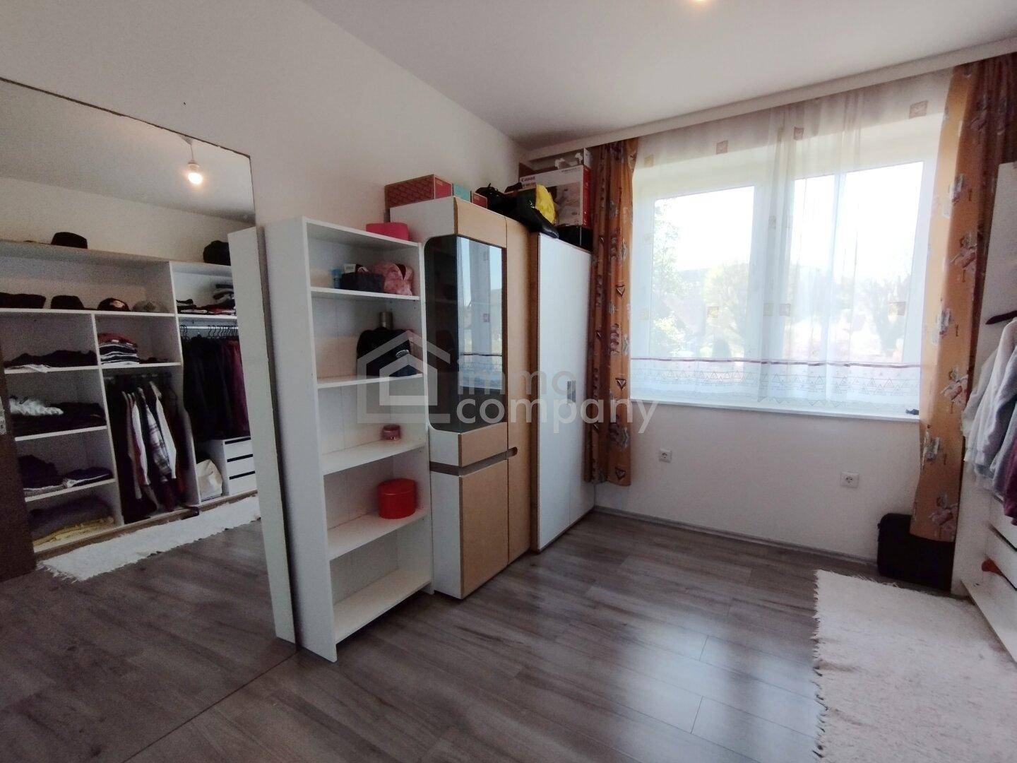 Schlafzimmer mit integriertem begehbarem Kleiderschrank und hellem Laminatboden.