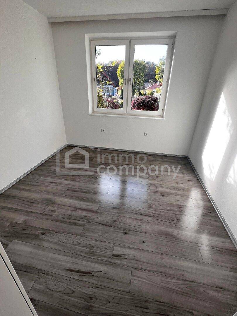 Helles Zimmer mit Laminatboden und großem Fenster, ideal als Schlaf- oder Arbeitszimmer.