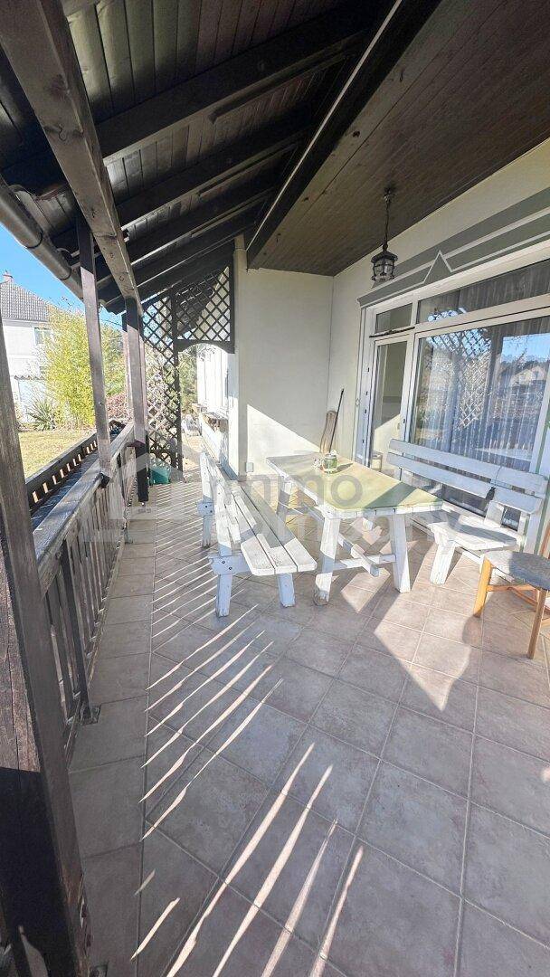 Überdachte Terrasse mit Fliesenboden und rustikalen Holzmöbeln für entspannte Stunden.