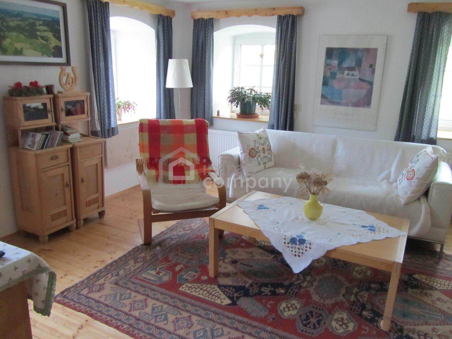 Gemütliches Wohnzimmer mit Holzboden, bequemer Couch und traditionellen Holzmöbeln, hell beleuchtet.