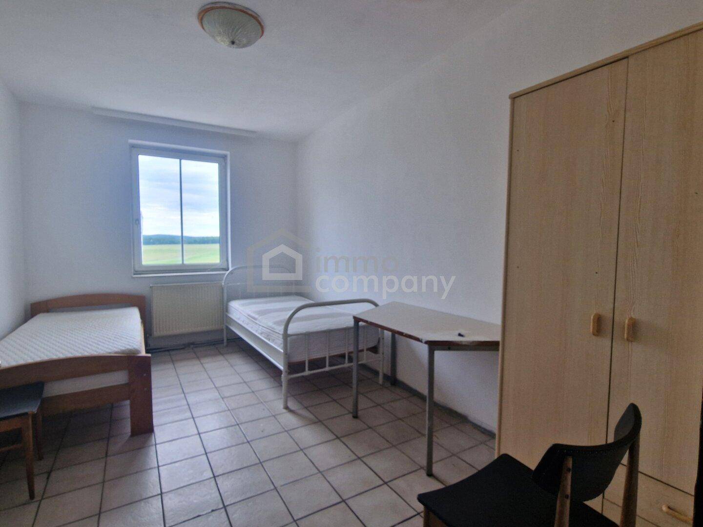 Einfaches Schlafzimmer mit zwei Einzelbetten, einem Tisch, Kleiderschrank und Fliesenboden mit Ausblick.