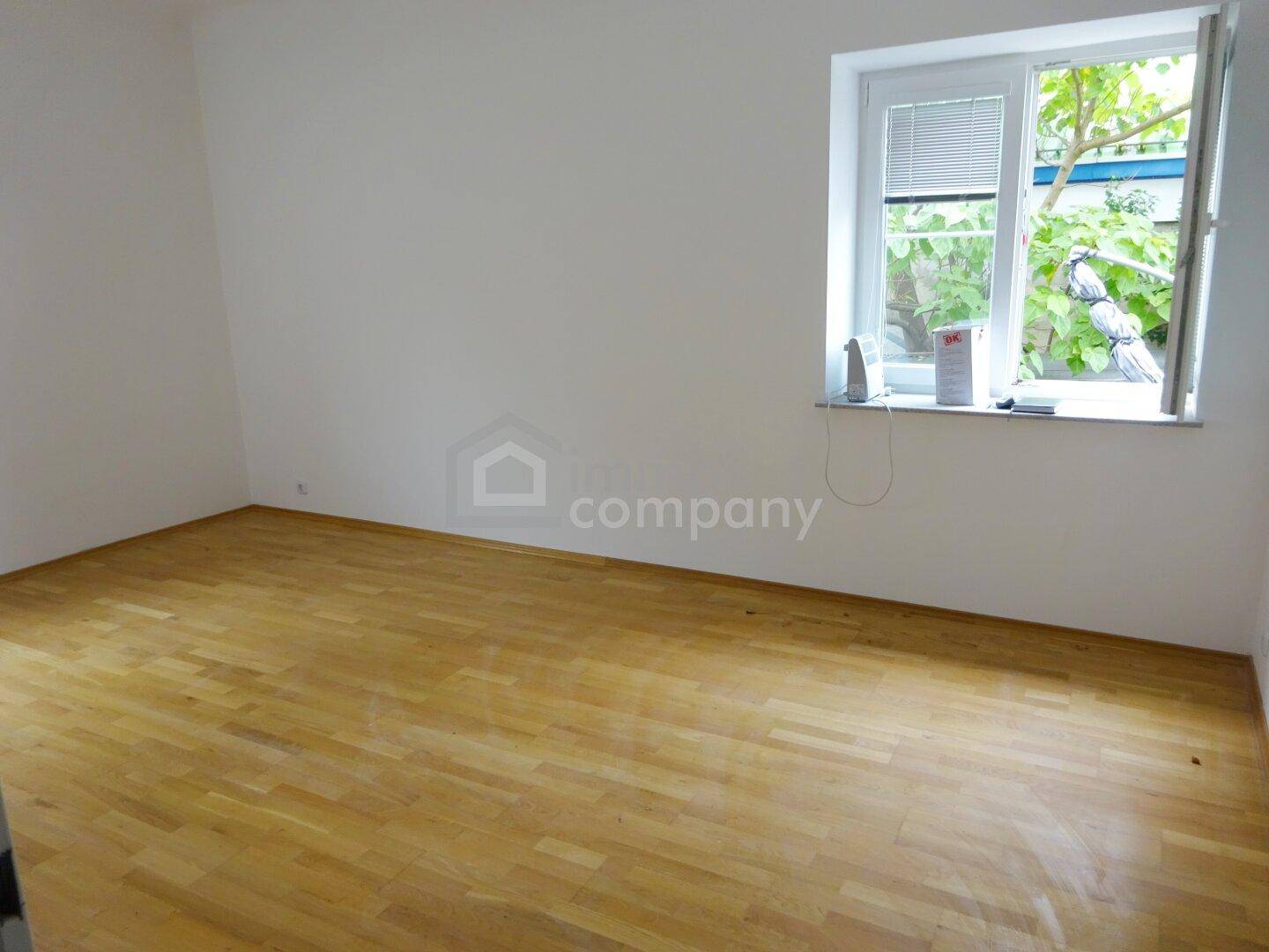 Freundliches Zimmer mit Holzboden und Blick ins Grüne durch das Fenster.