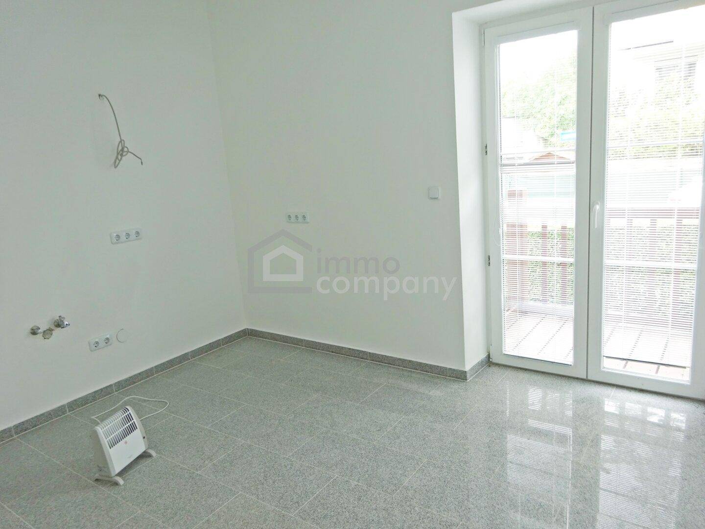 Heller Raum mit Fliesenboden und Zugang zu einem Balkon oder einer Terrasse.