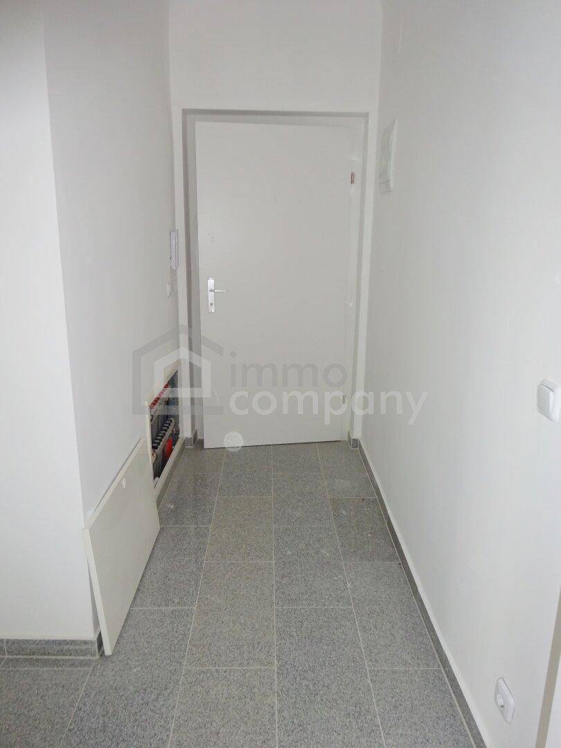 Heller Flur mit Fliesenboden und Zugang zur Wohnung, inklusive Sicherungskasten.