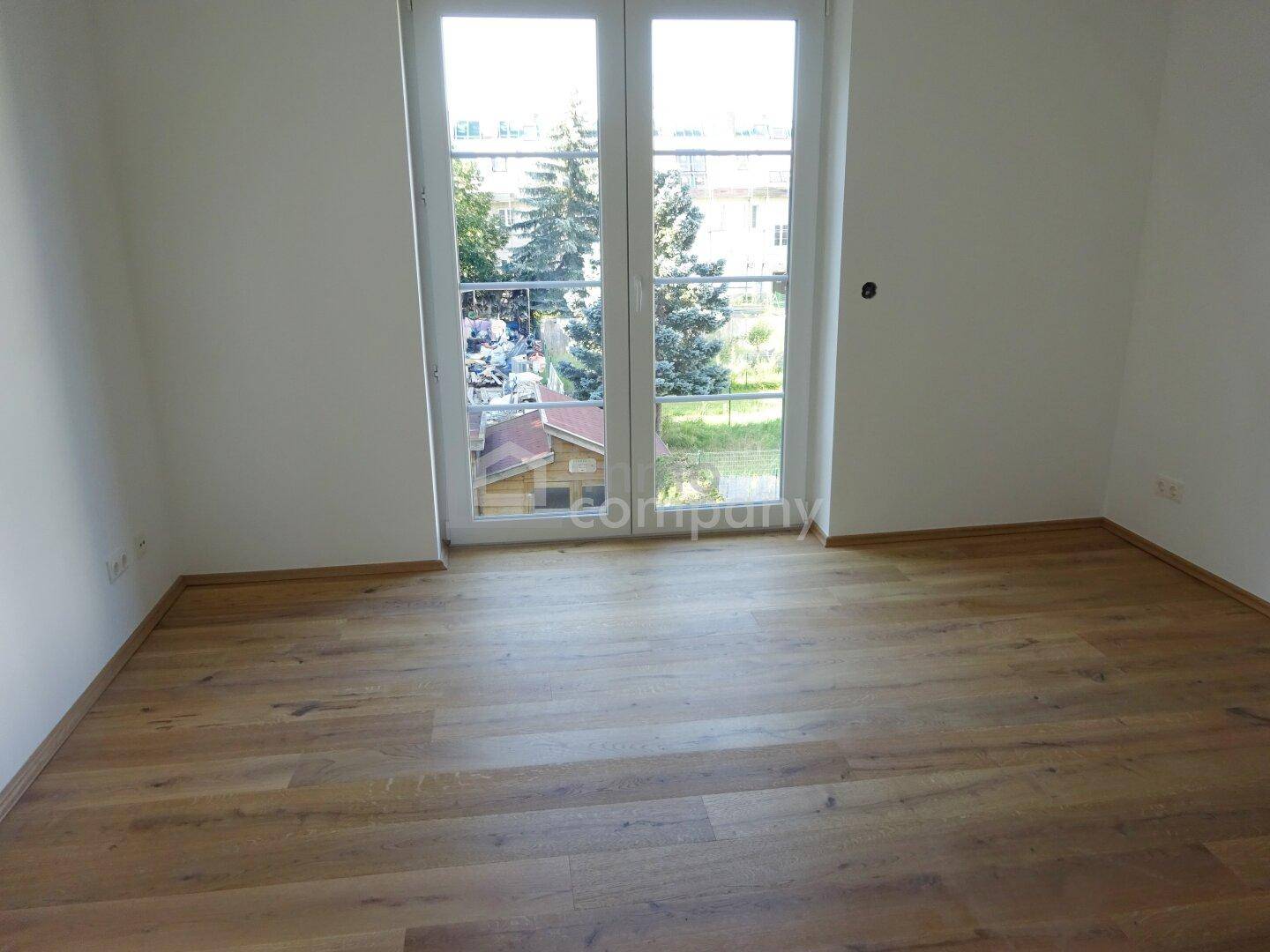Heller Raum mit Holzboden und großen Fenstertüren, die Zugang zu einem französischen Balkon oder einer kleinen Terrasse bieten.