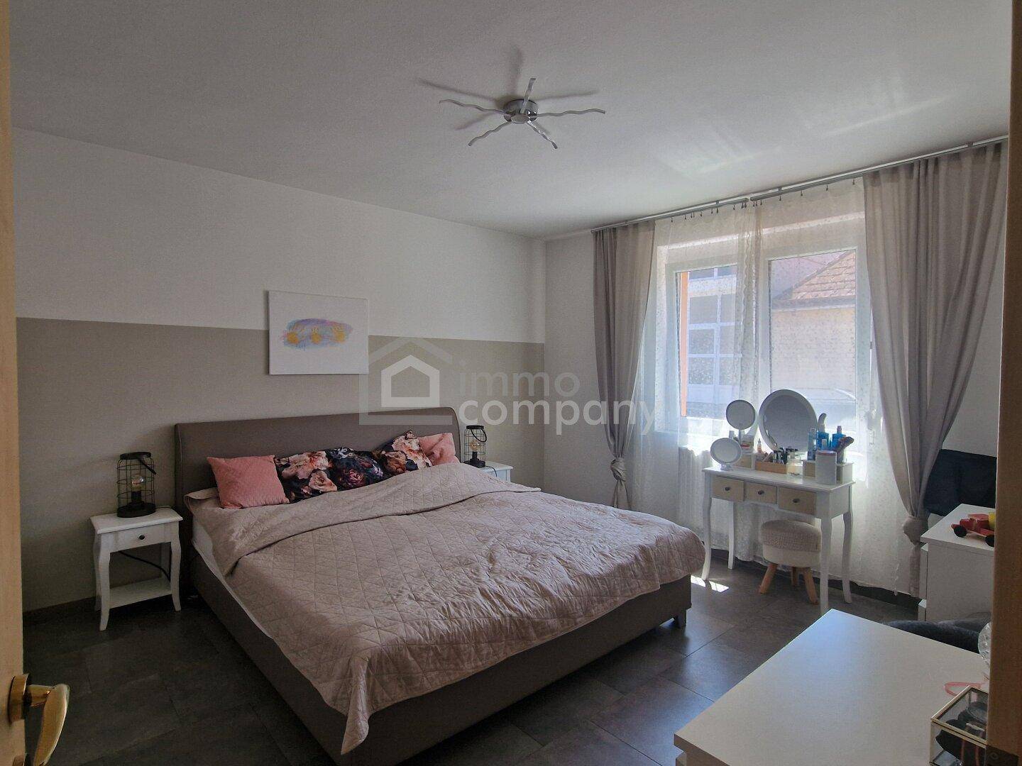 Gemütliches Schlafzimmer mit großem Bett, Schminktisch und Fenster mit Vorhängen.