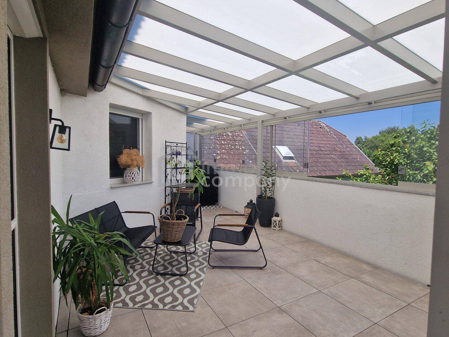 Überdachter Außenbereich mit Glasdach, Fliesenboden und bequemen Sitzgelegenheiten.