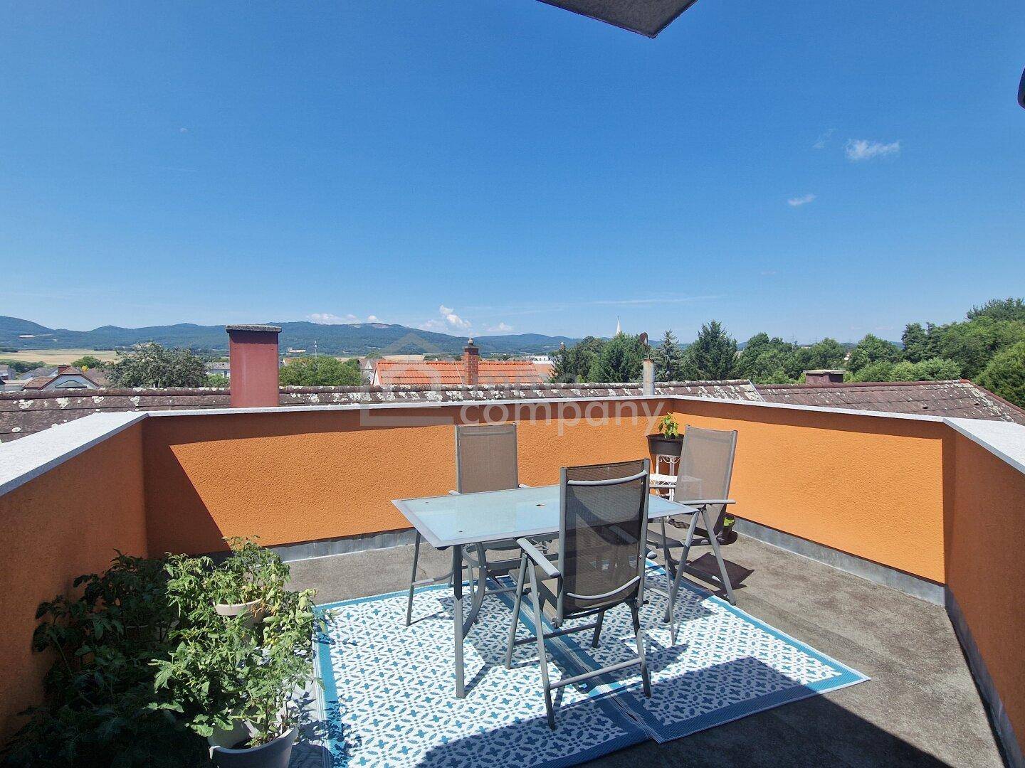 Sonnige Dachterrasse mit Gartenmöbeln und weitem Blick auf die umliegende Landschaft.