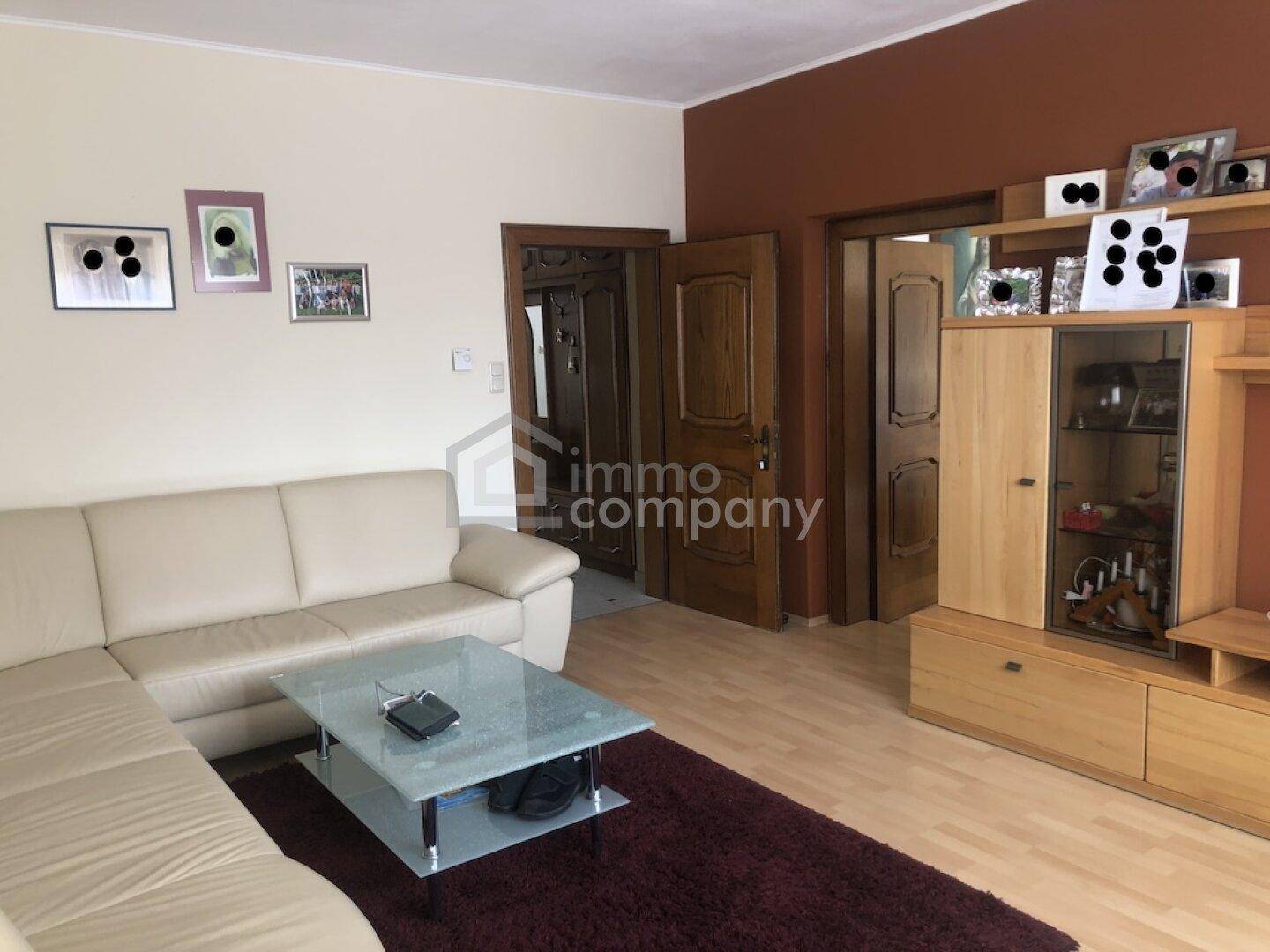 Gemütliches Wohnzimmer mit beigem Sofa, Holzboden und dekorativen Elementen an den Wänden.