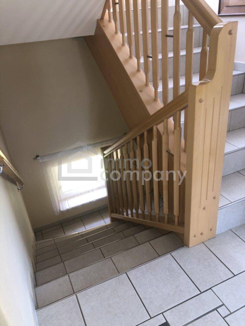 Treppenhaus mit Holzgeländer und gefliesten Stufen, führt zu den unteren Etagen des Hauses.